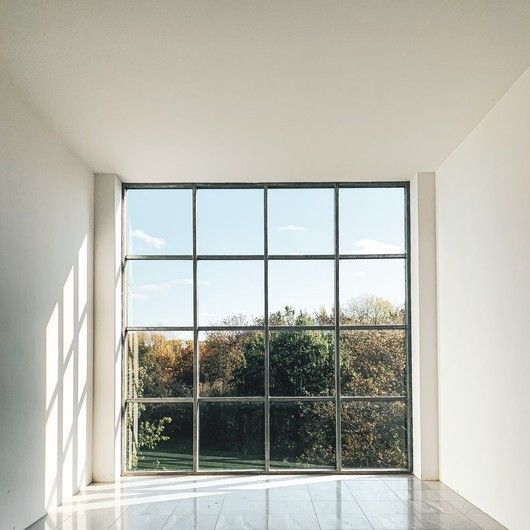 Bright empty room with large floor-to-ceiling window overlooking trees and blue sky