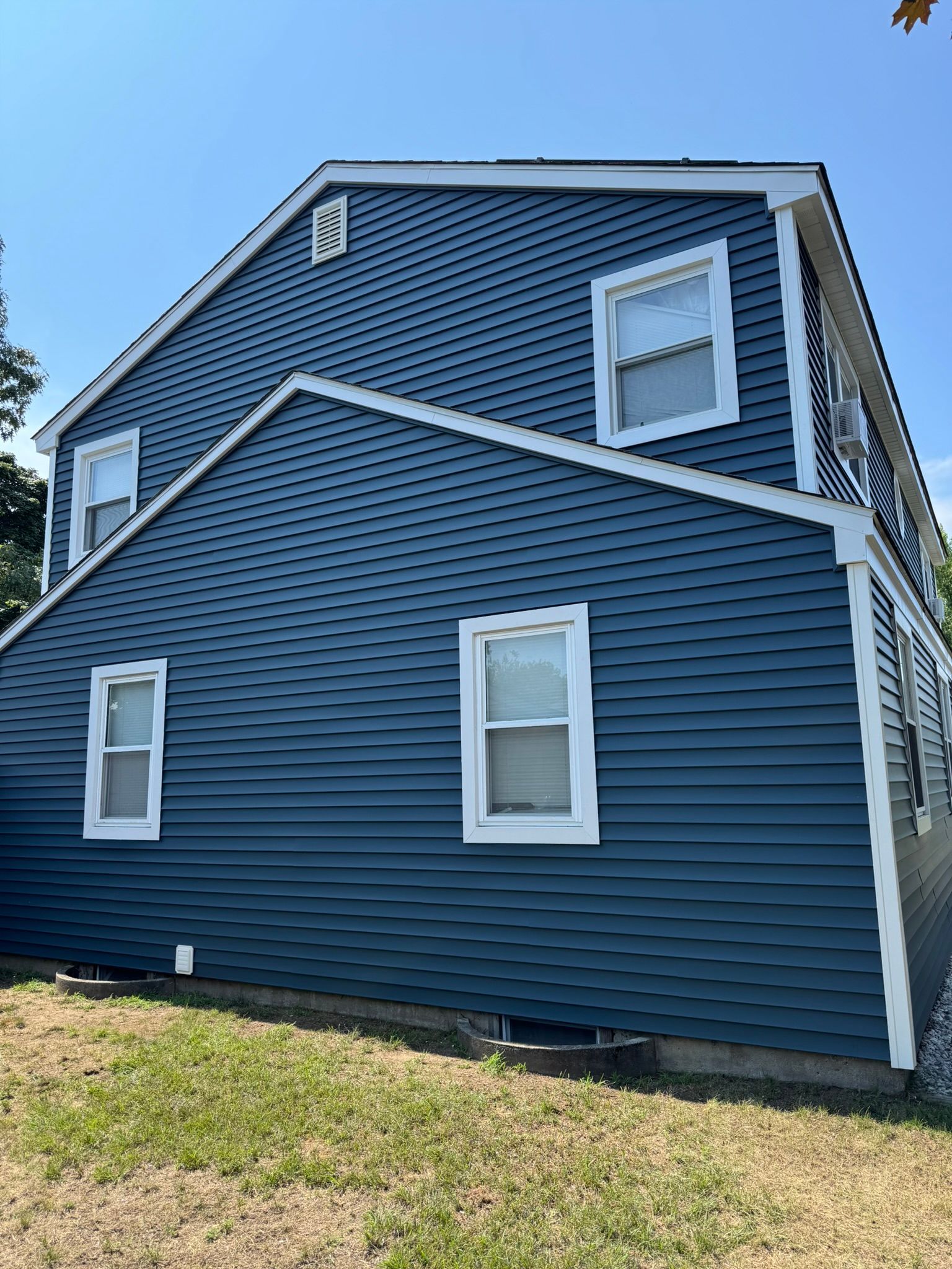 Blue house exterior with white-trimmed windows and a sloped roof, viewed from the side.