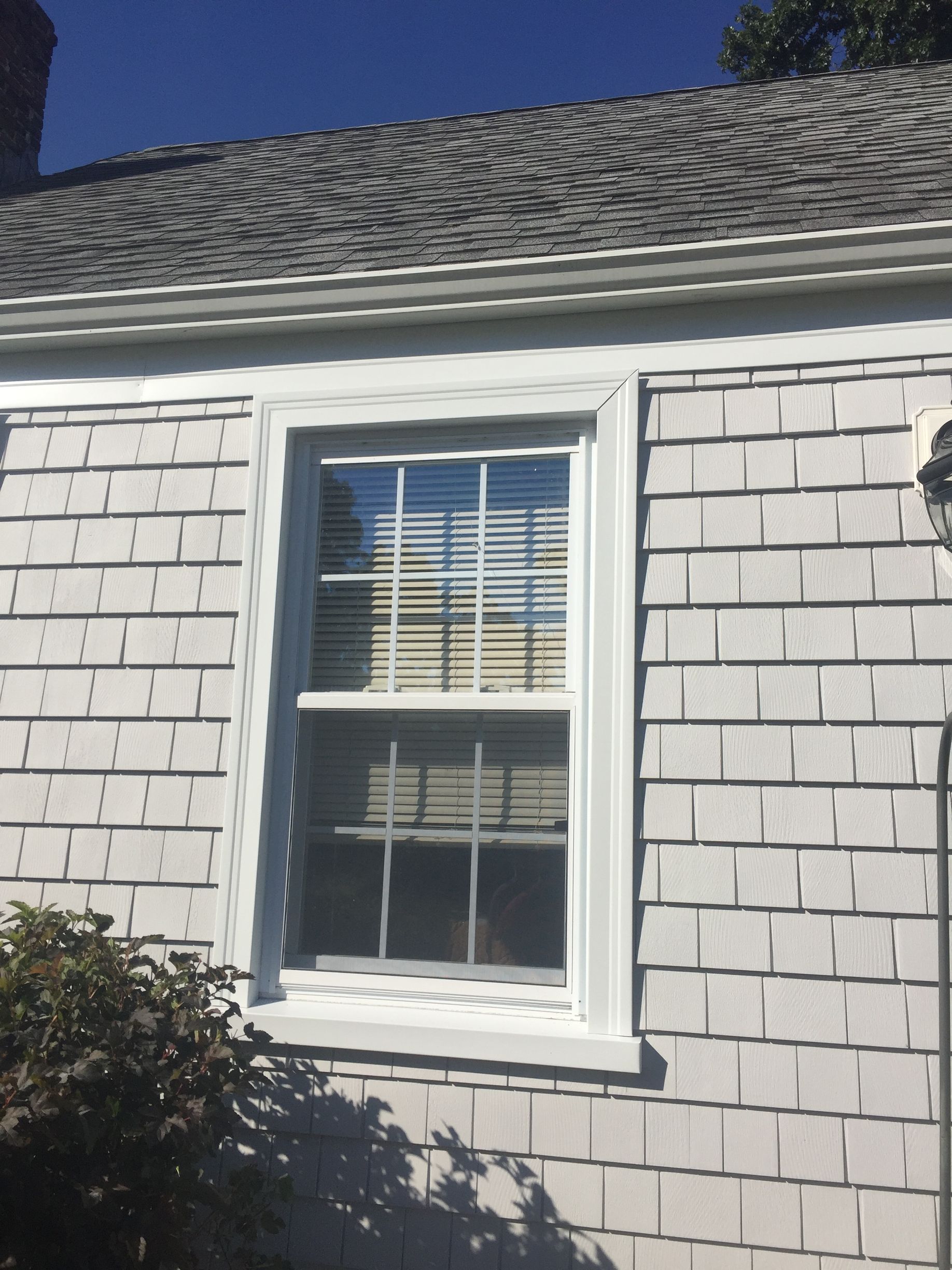 White house exterior with a double-hung window and black roof shingles under a blue sky