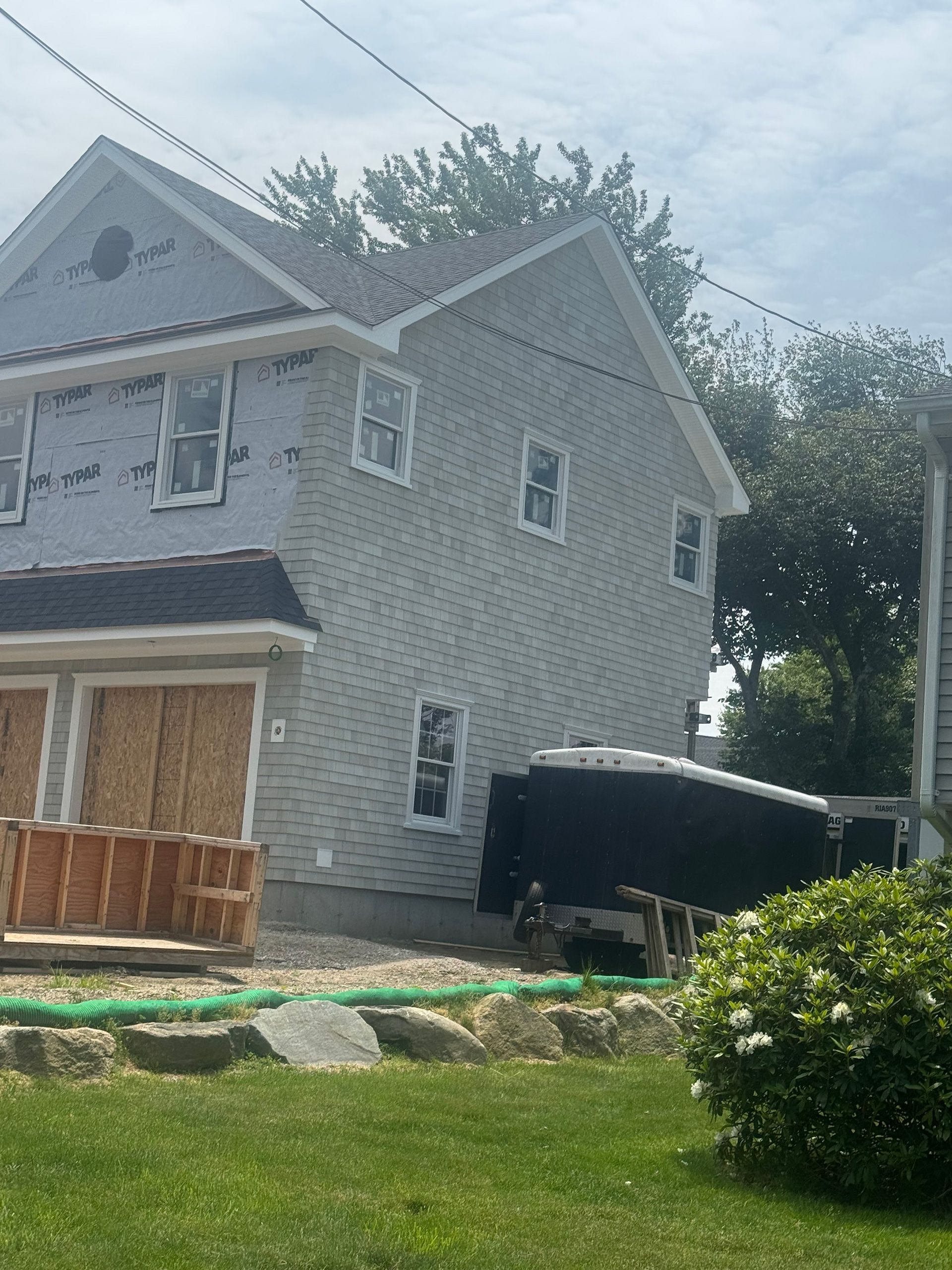 Gray two-story house with light trim, unfinished porch, and a green lawn in front