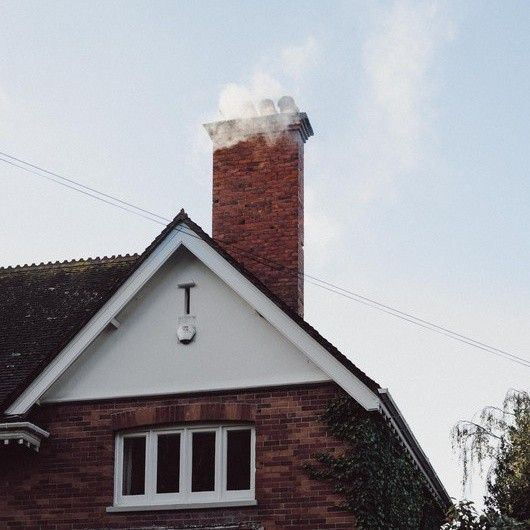 Brick house chimney releasing smoke against a pale sky