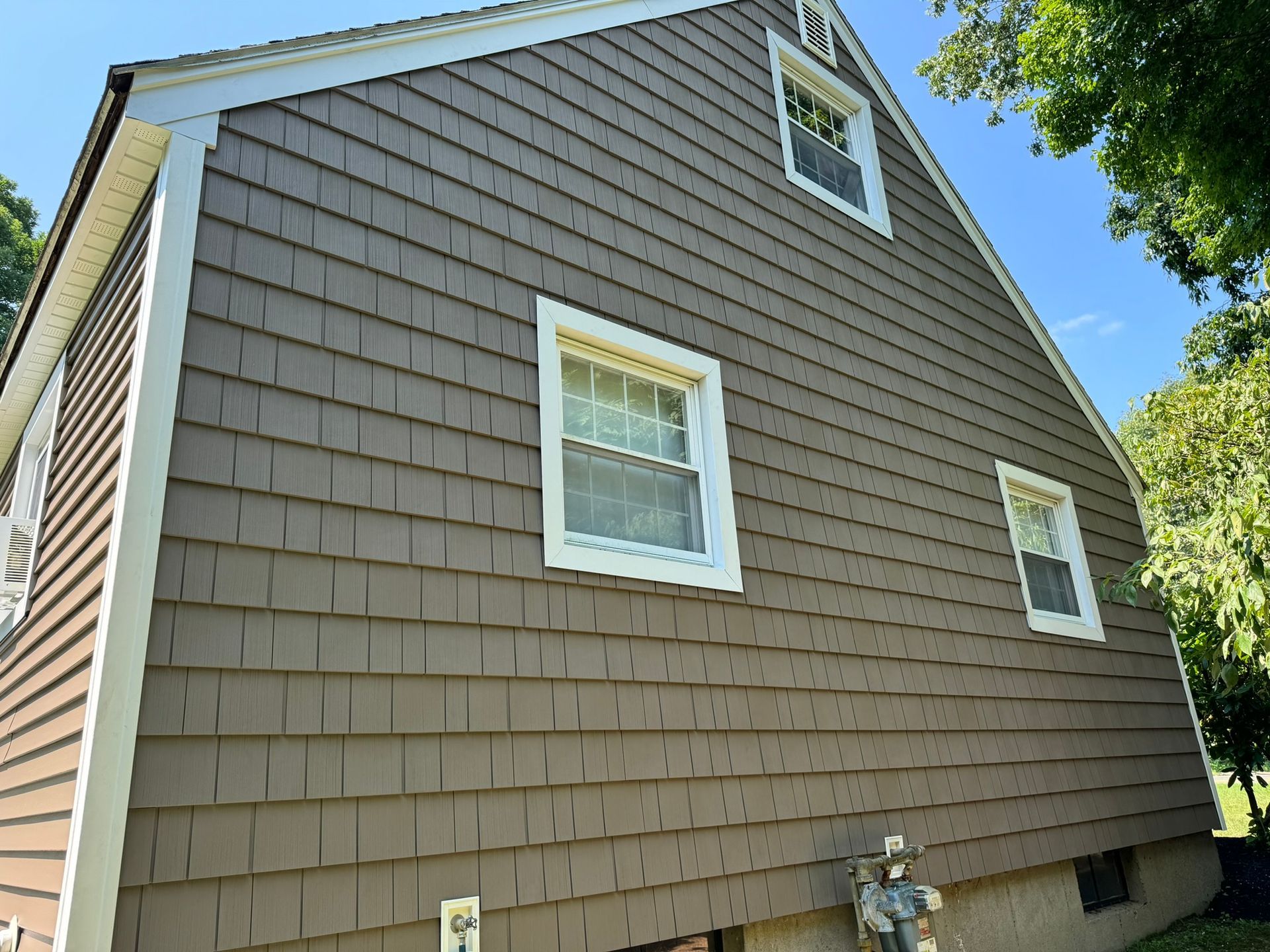 Brown house exterior with white-trimmed windows and shingled siding under a blue sky