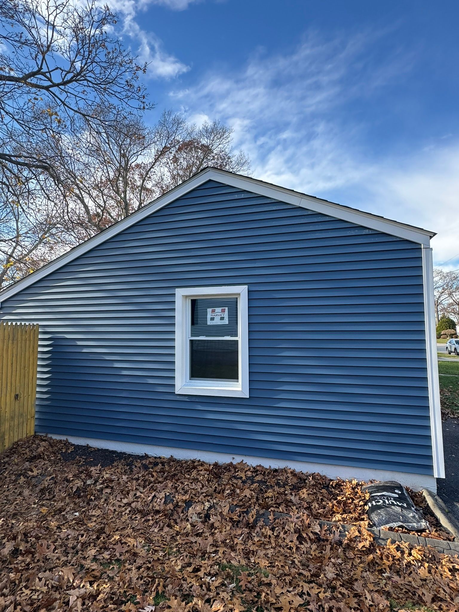 Blue house exterior with a small window, white trim, and leaf-covered ground in front