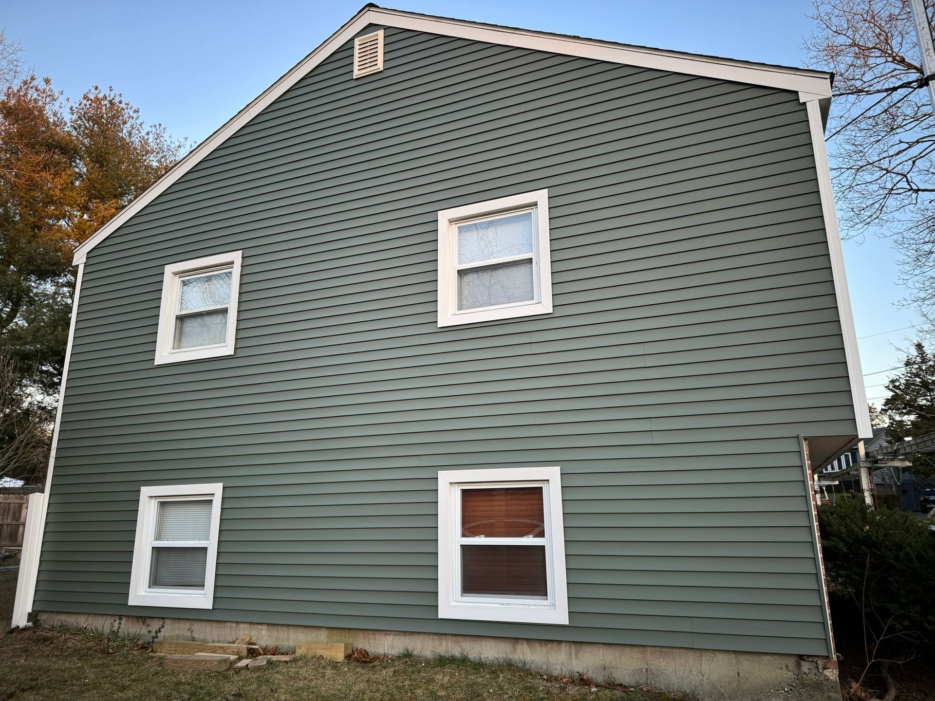 Blue-gray house with white-trim windows and siding, seen from the side under a clear sky