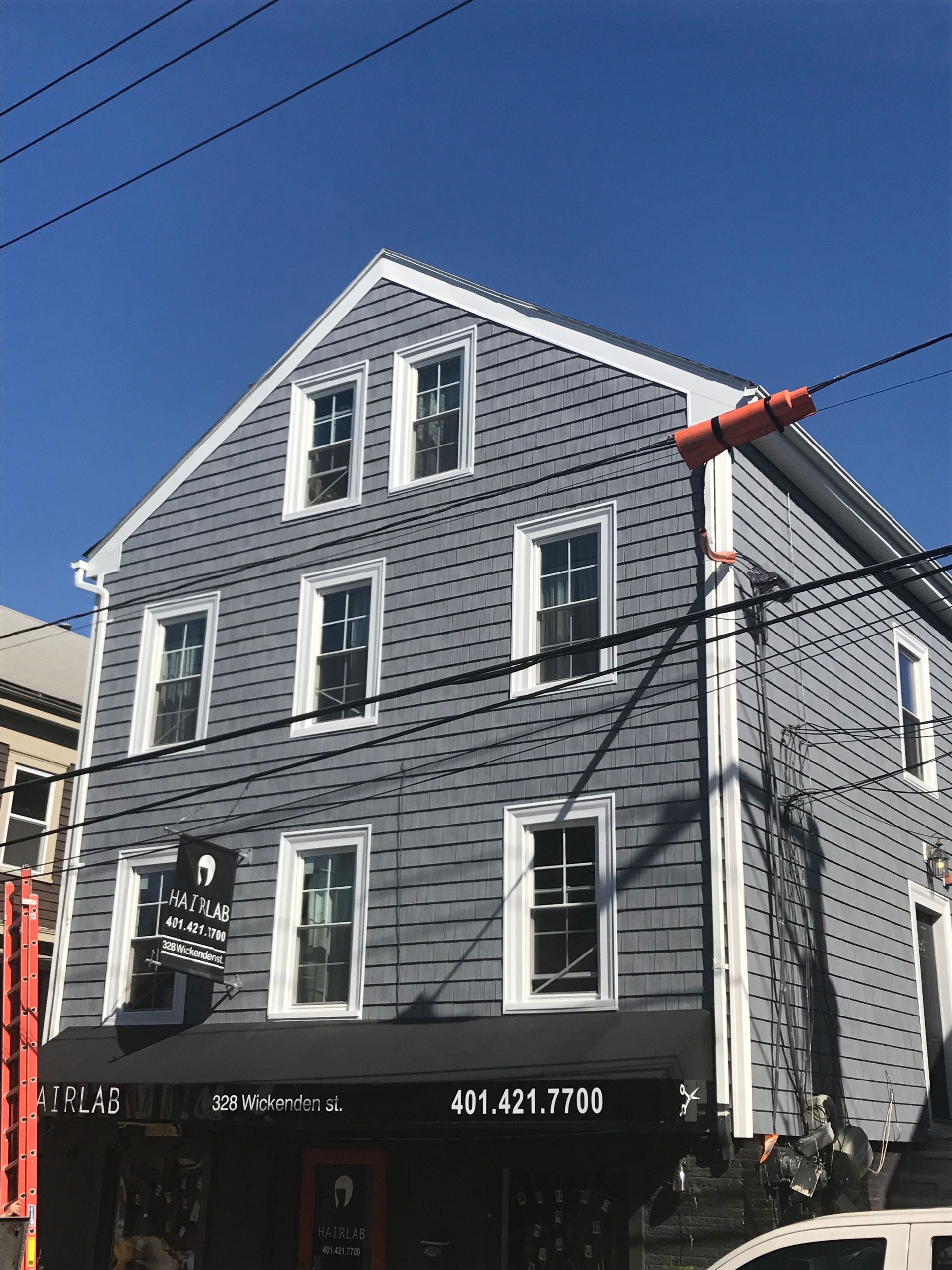Gray three-story house with white trim and black storefront under a blue sky, viewed from the street