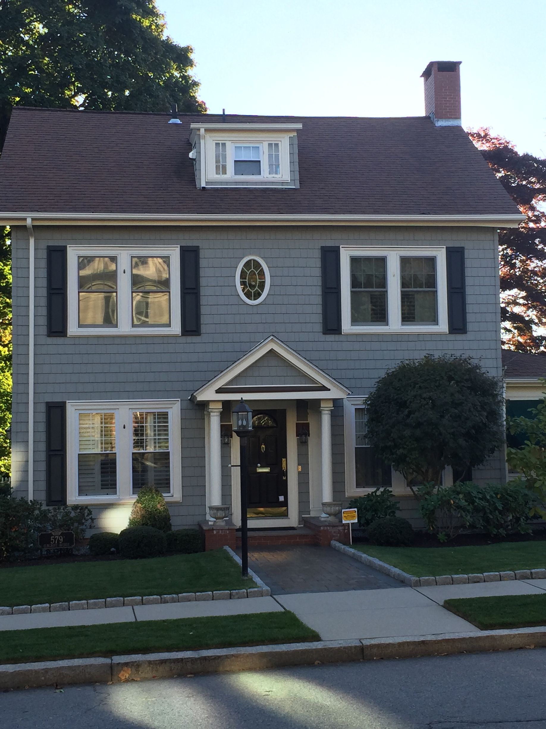 Two-story gray house with white trim, a small front porch, and a sidewalk in front.
