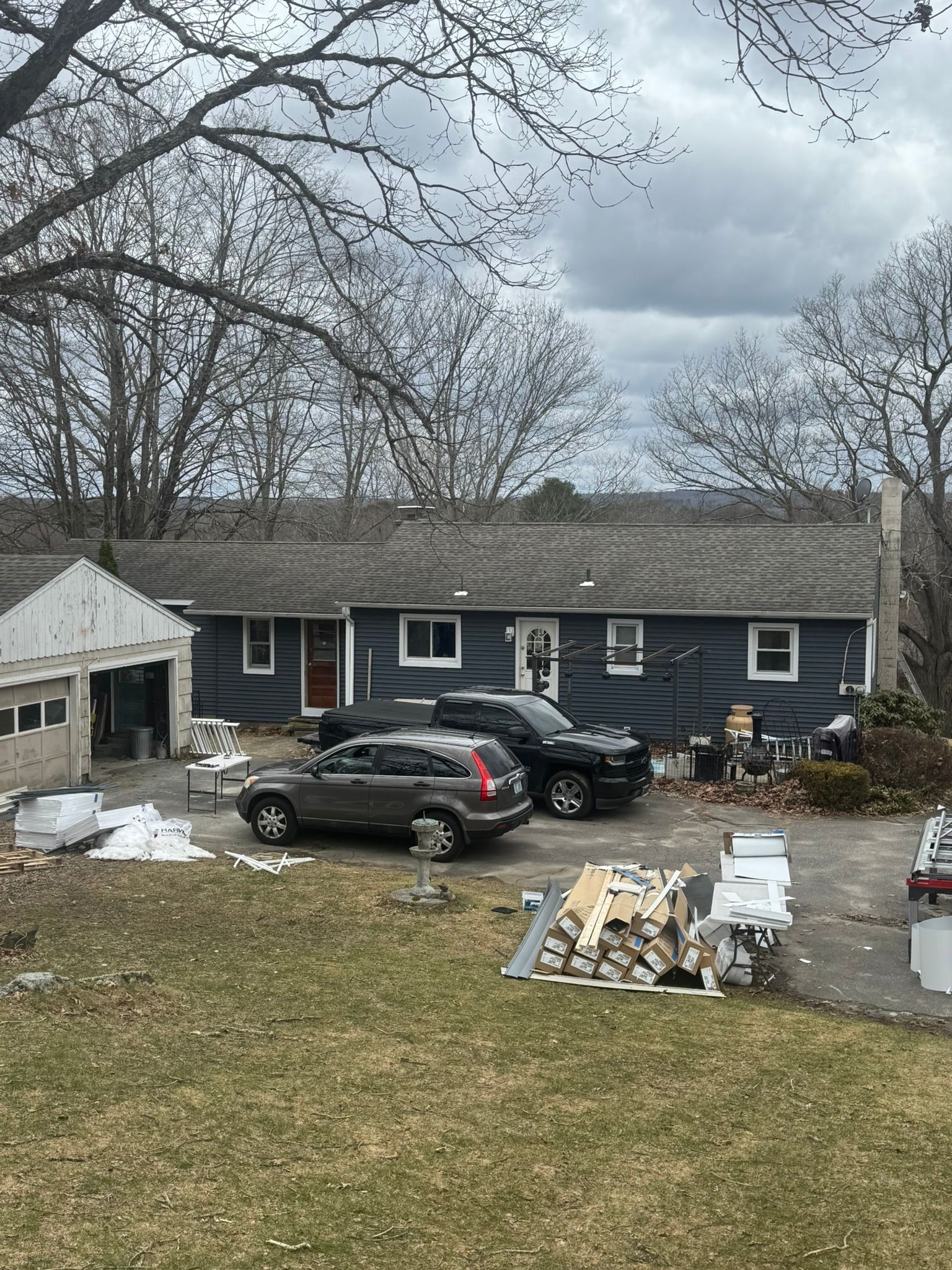 Dark blue house with cars in driveway, piles of debris in yard, and bare tree branches overhead