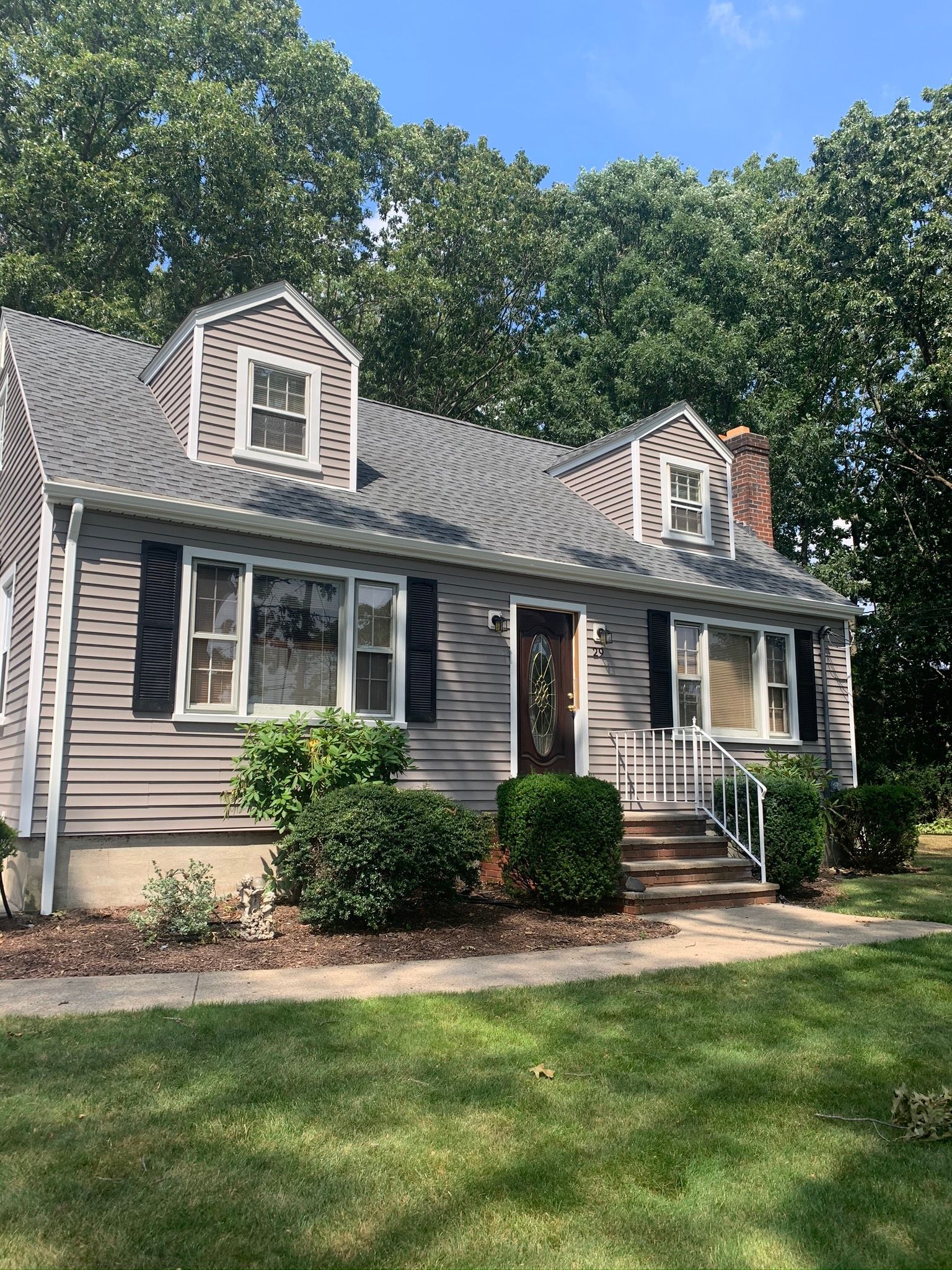 Suburban house with gray siding, dormer windows, and a front lawn under a blue sky