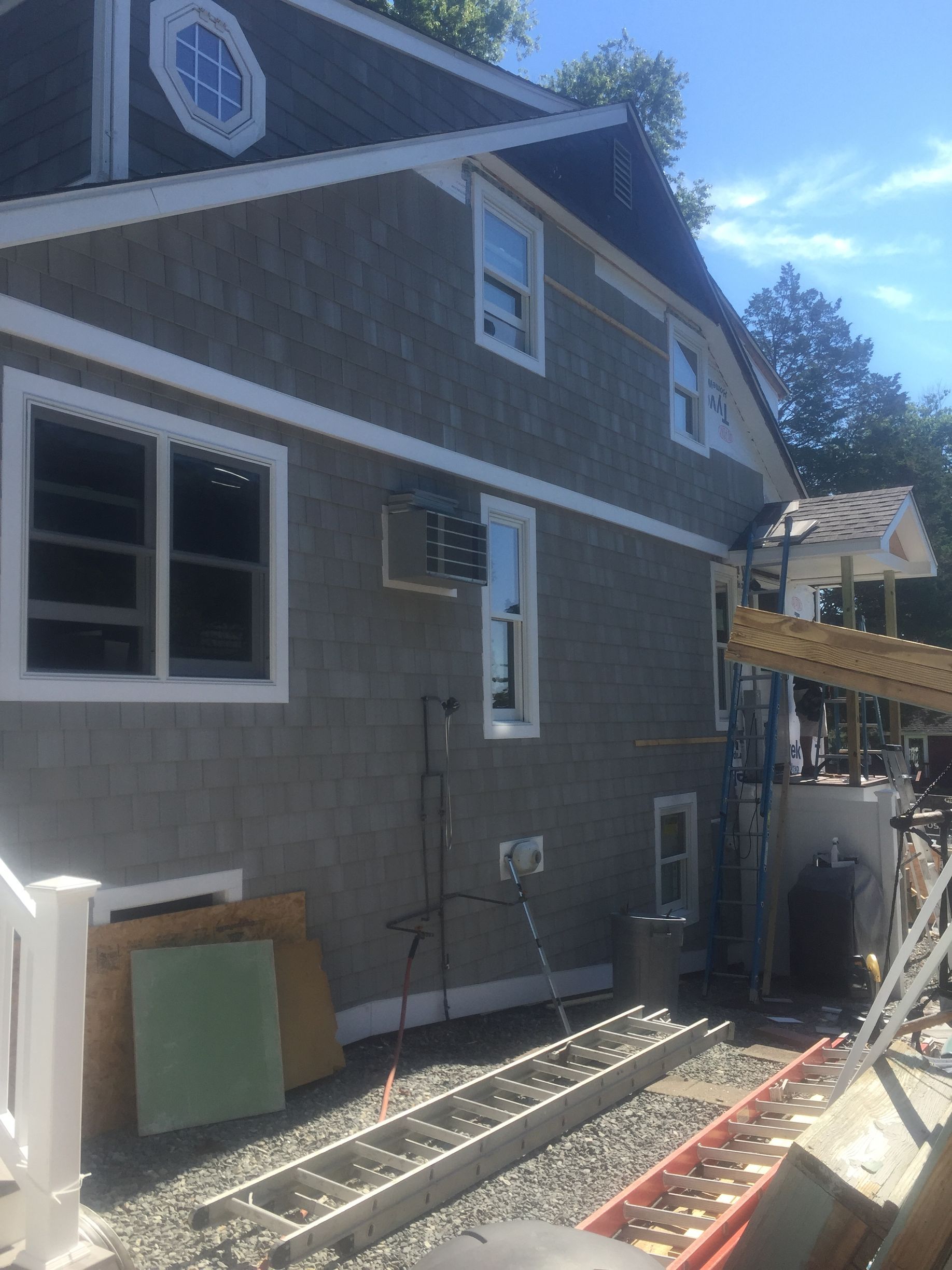 House exterior under construction with gray siding, white-trimmed windows, and building materials on the ground
