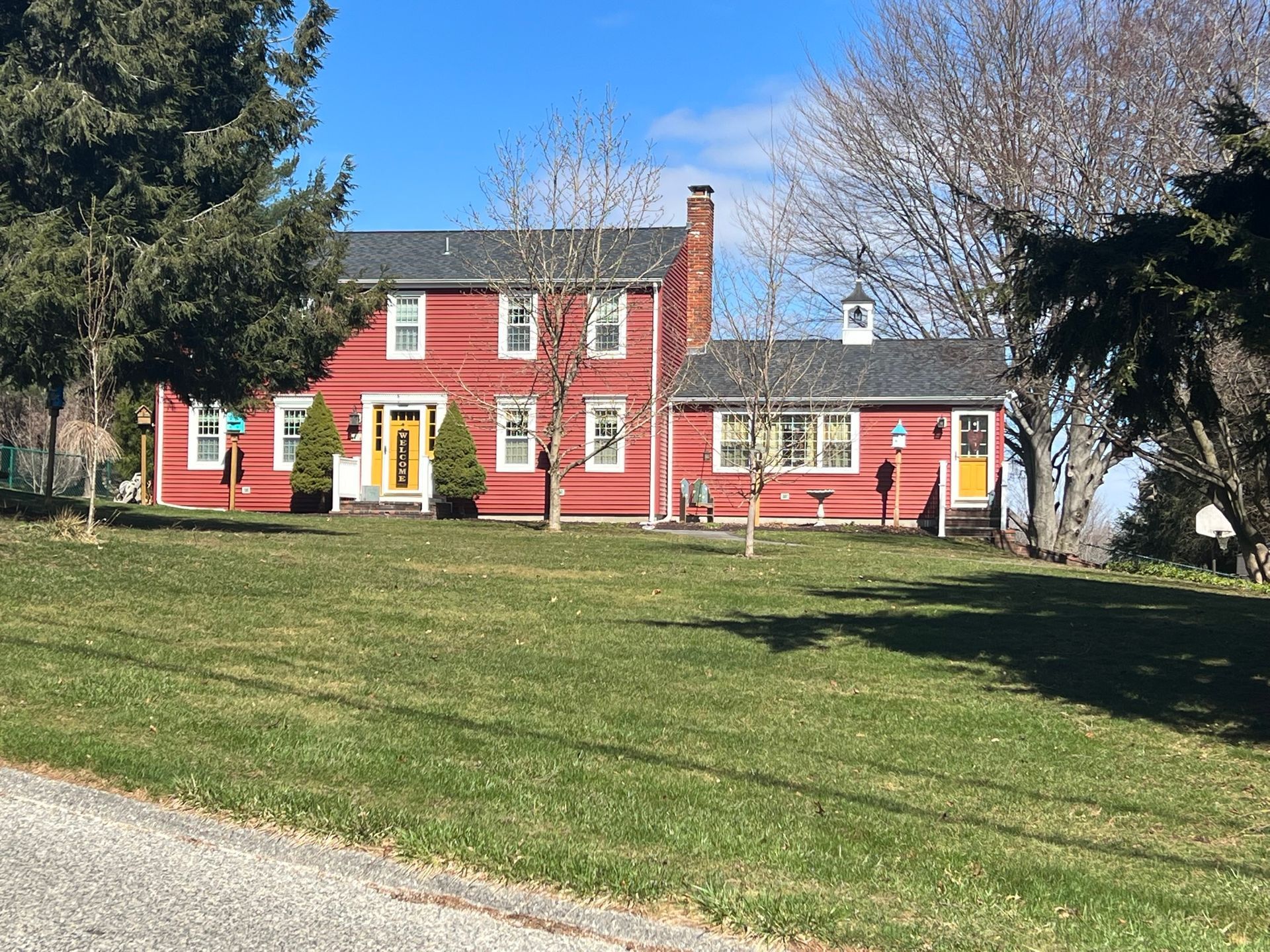 Red colonial-style house with white trim and yellow doors on a grassy lawn under a clear sky