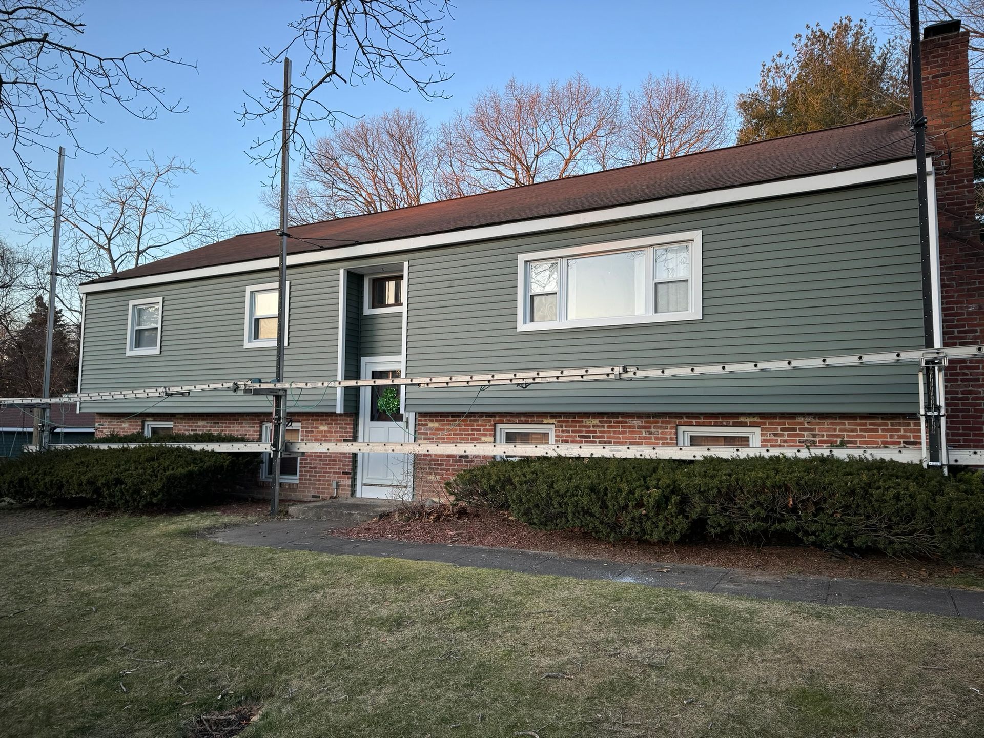 Green single-story building with white windows, brick steps, and shrubs in front, viewed from a lawn