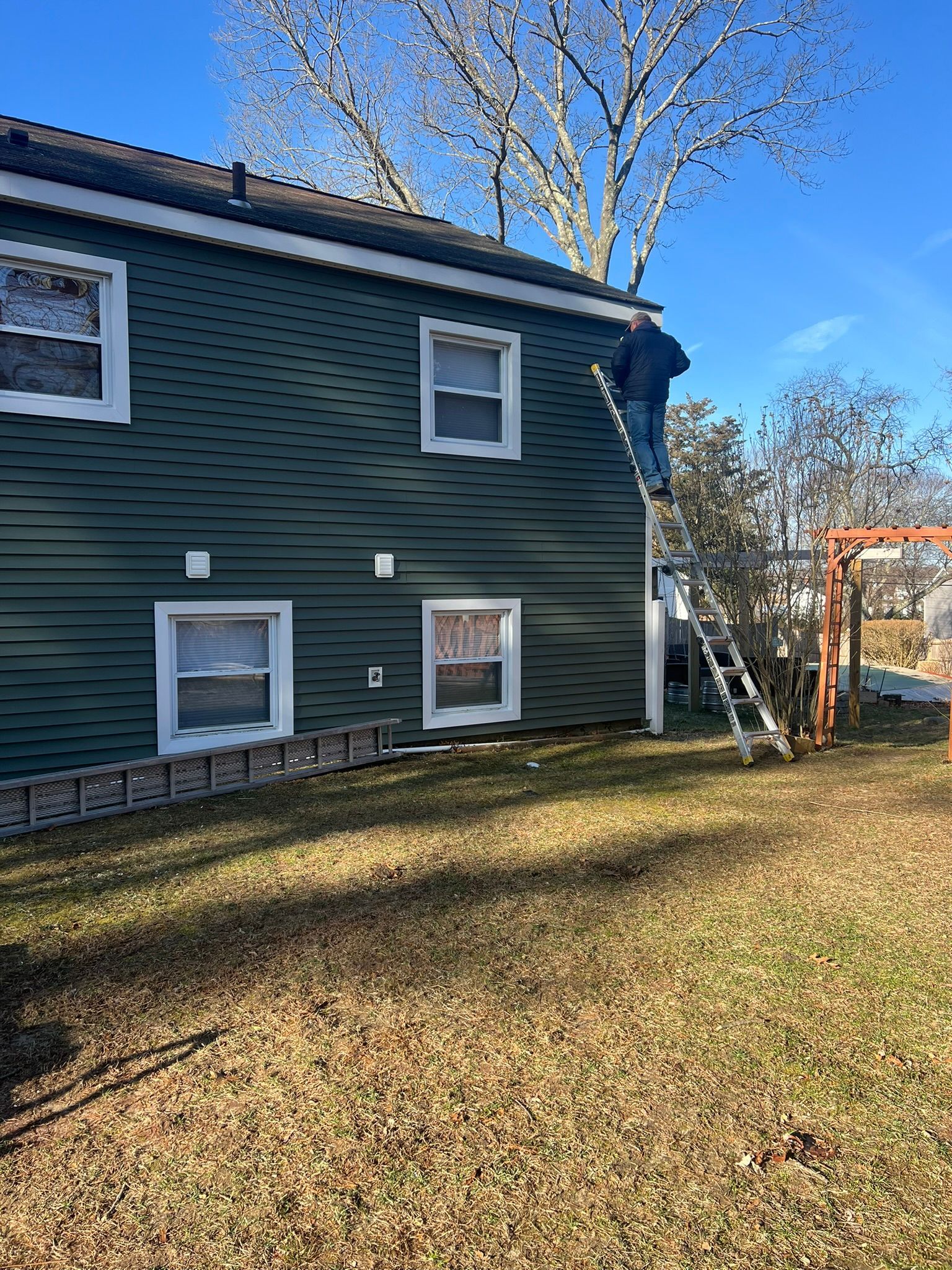 Dark green house exterior with white-trimmed windows and a leaf-covered yard under a blue sky