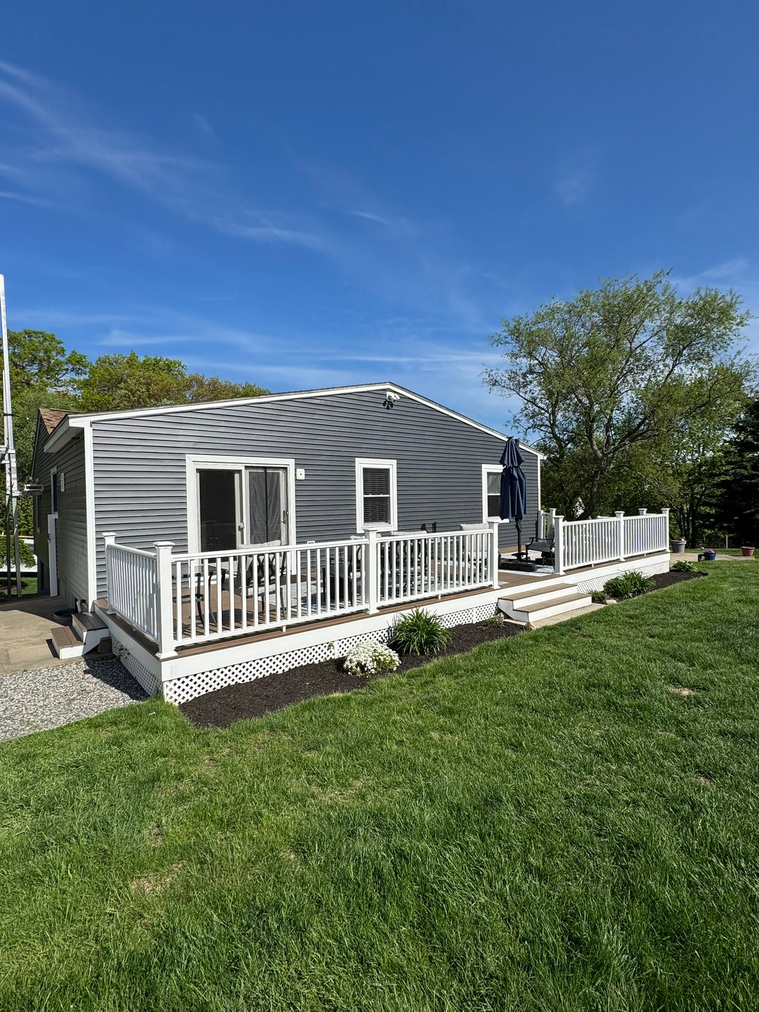 Small white house with a porch and railing on a grassy lawn under a blue sky.