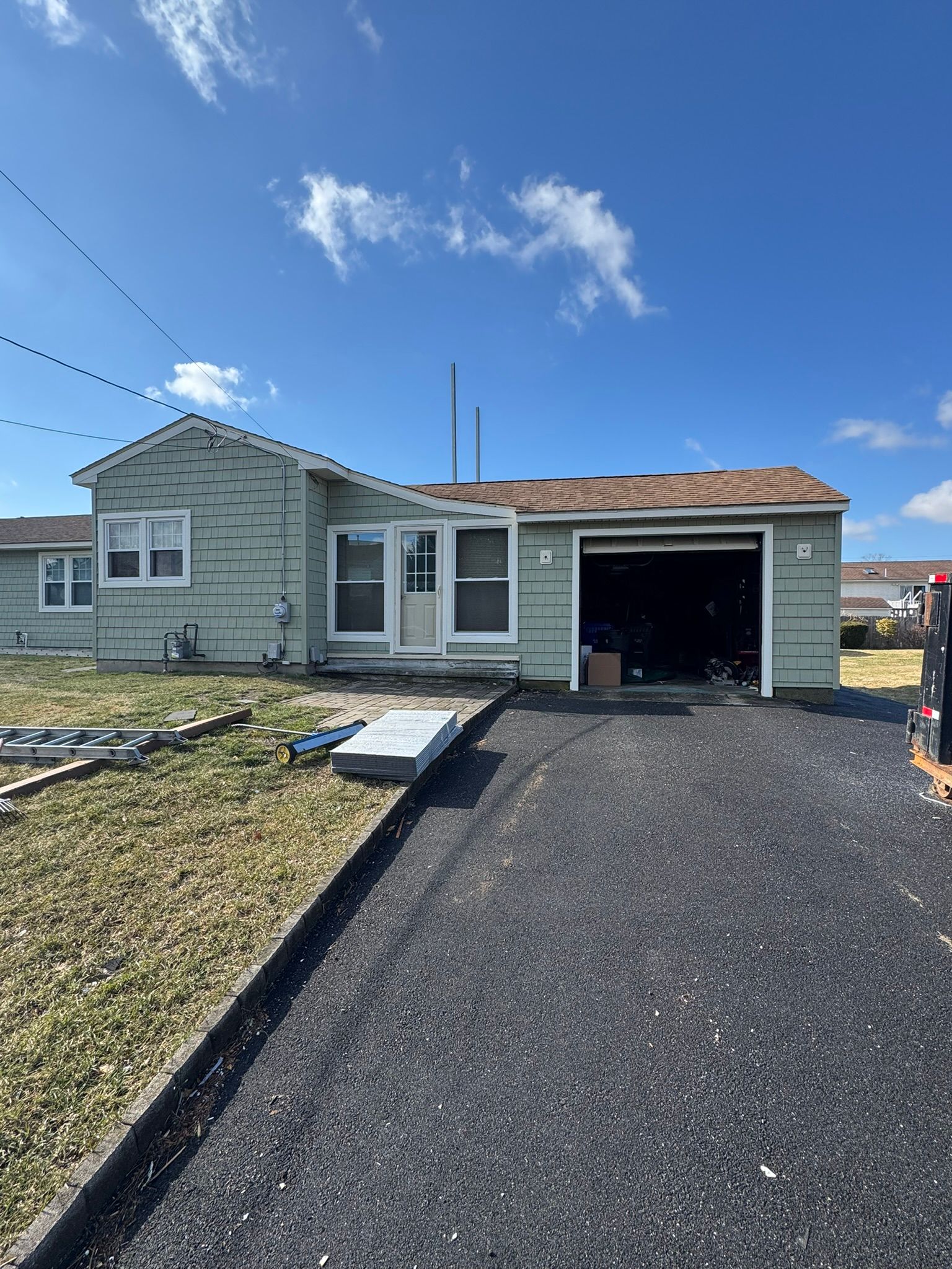 Single-story house with gravel driveway and open garage under a blue sky