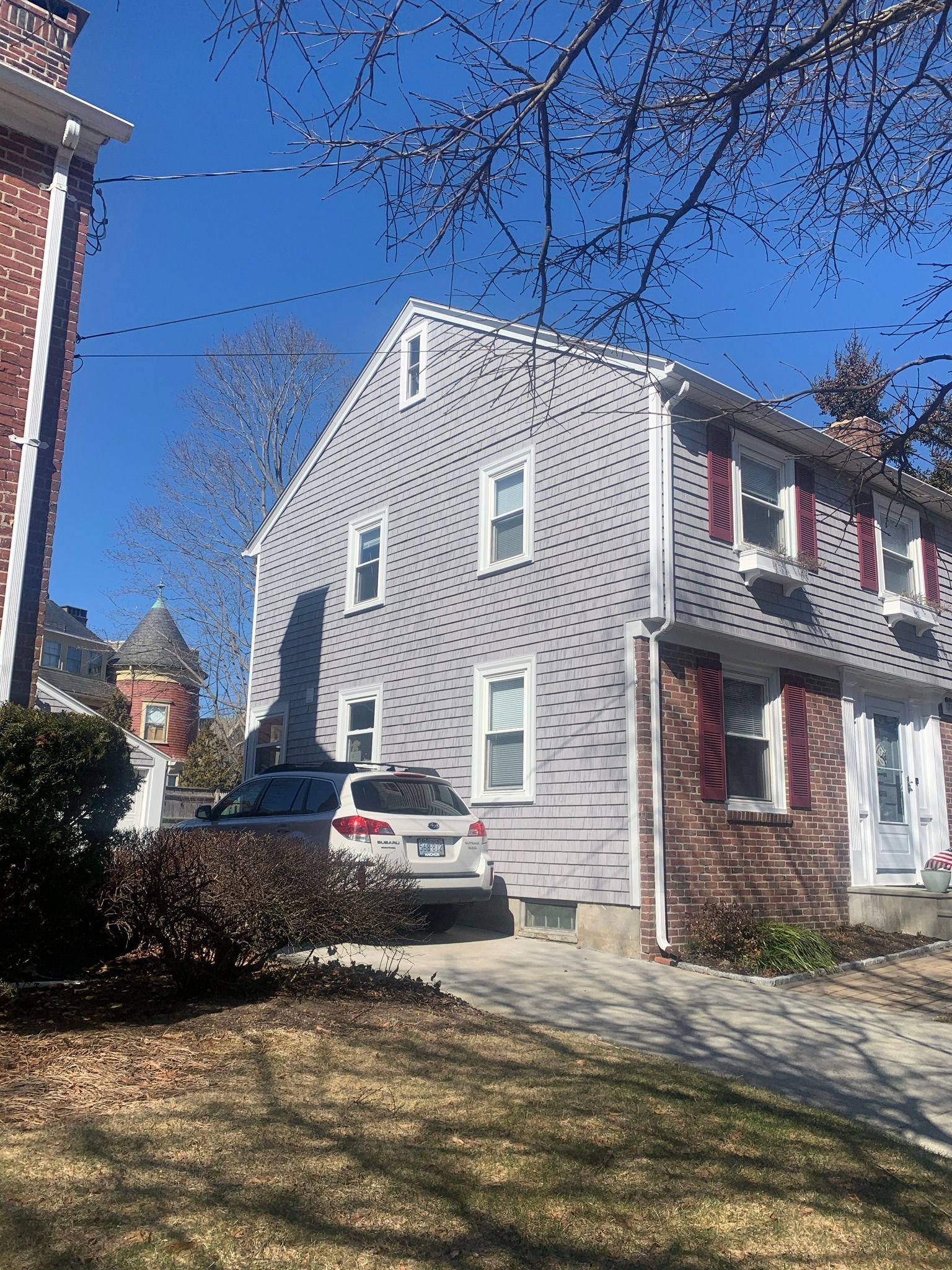 Gray two-story house with red shutters and a white car parked in the driveway on a sunny day