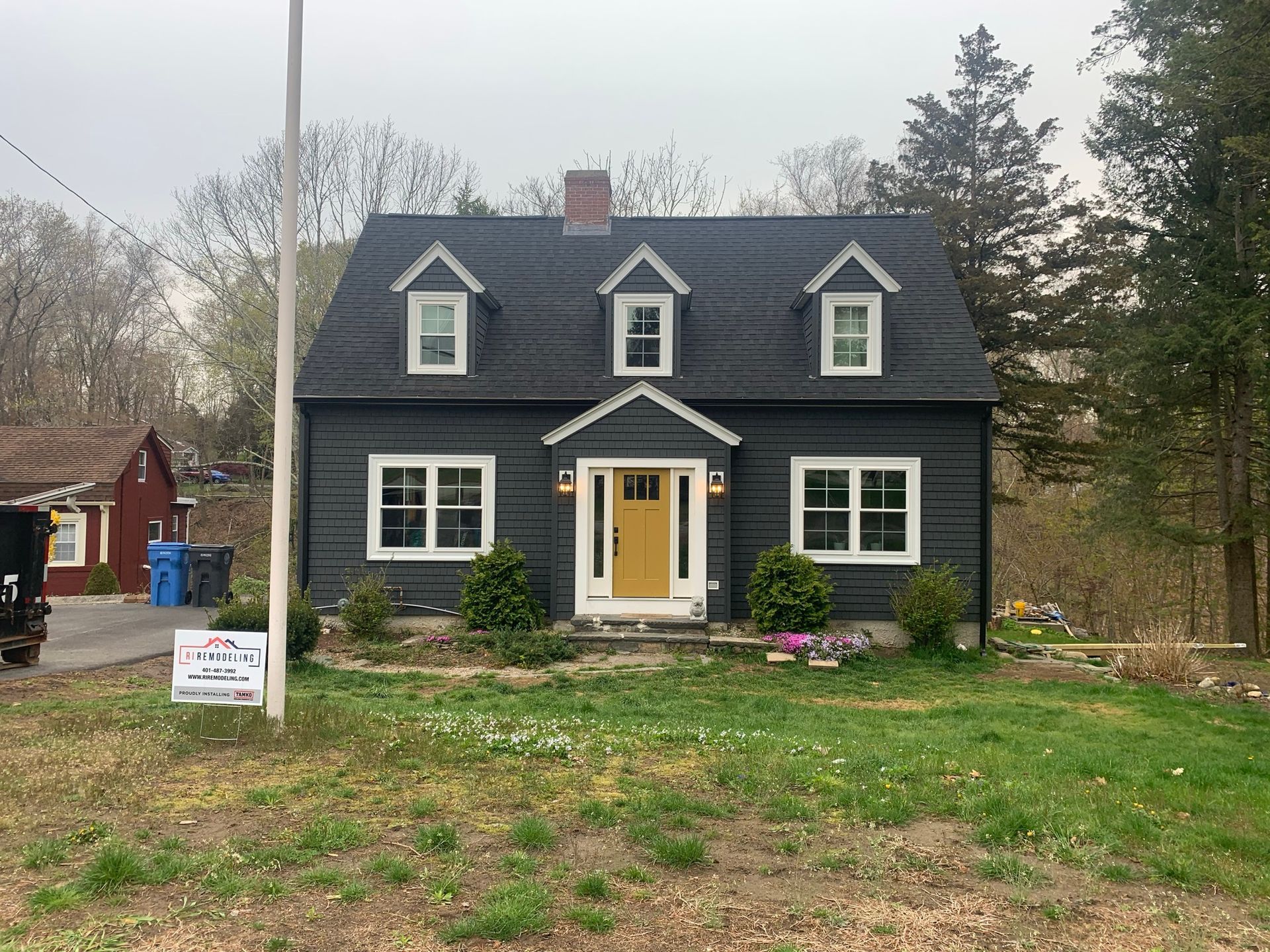 Gray two-story house with white trim, yellow door, and a front lawn on a cloudy day