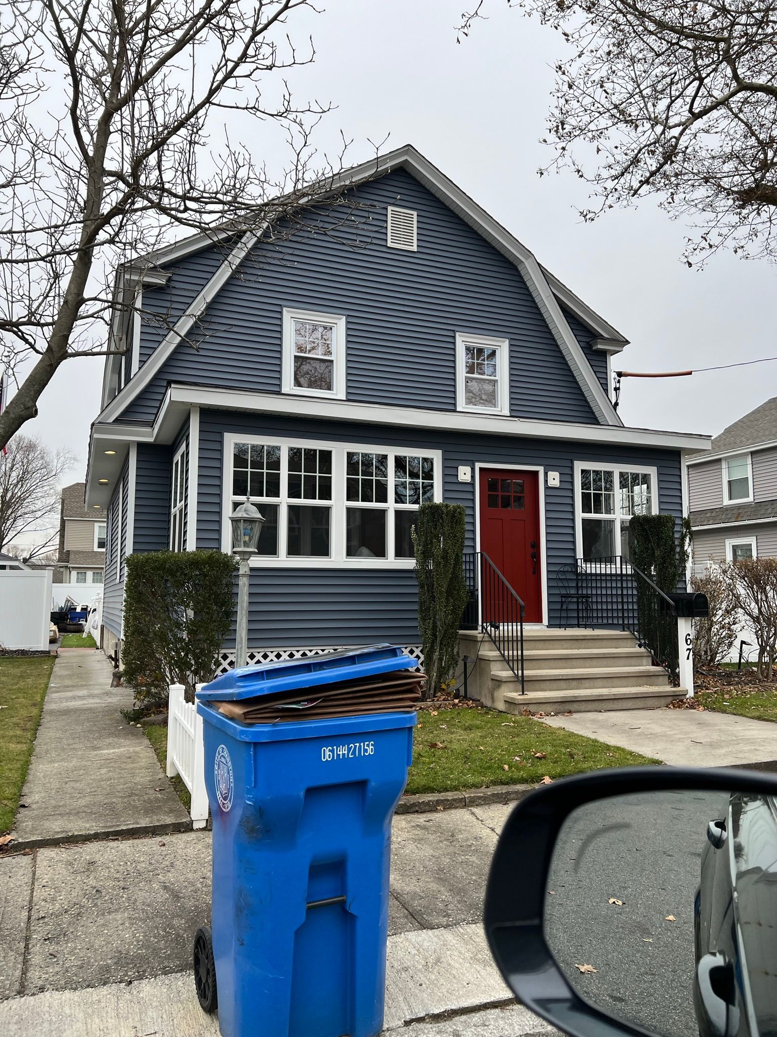 Blue two-story house with white trim, red front door, and a blue recycling bin by the curb