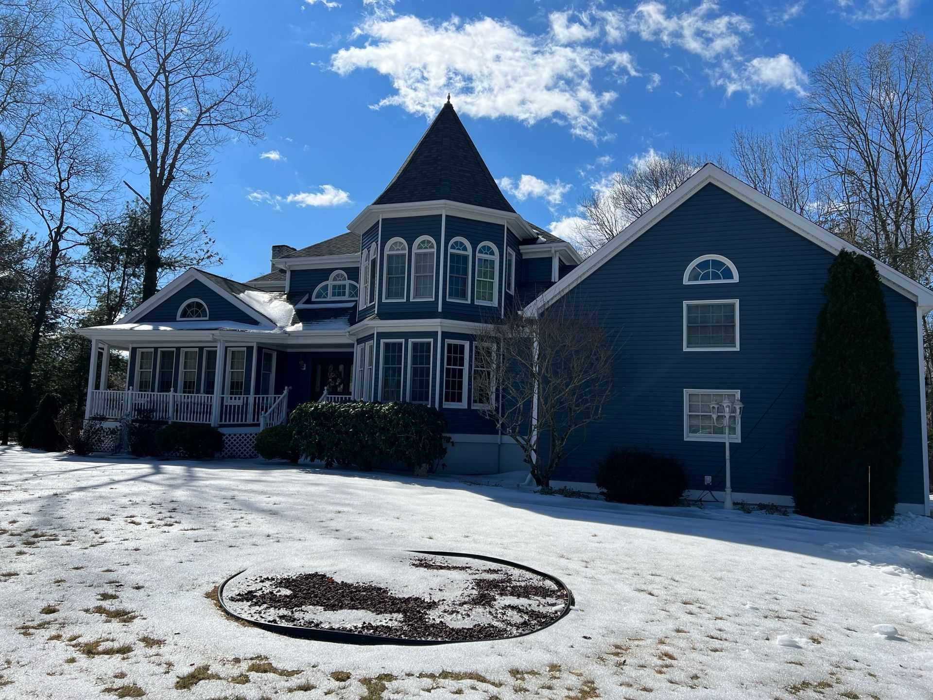 Large blue Victorian-style house with a turret in a snowy yard under a bright blue sky