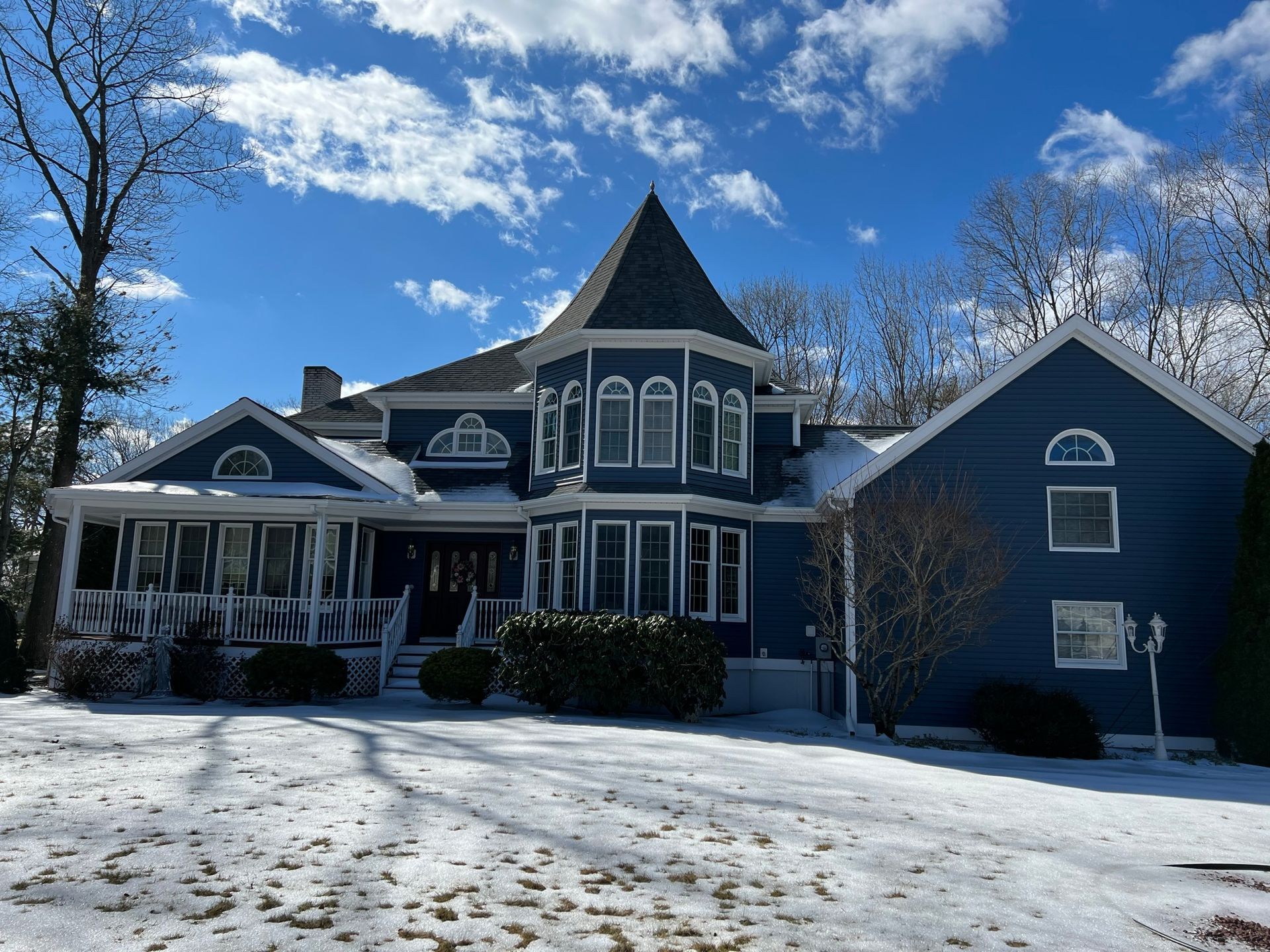 Snow-covered Victorian-style house with a turret under a blue sky on a winter day
