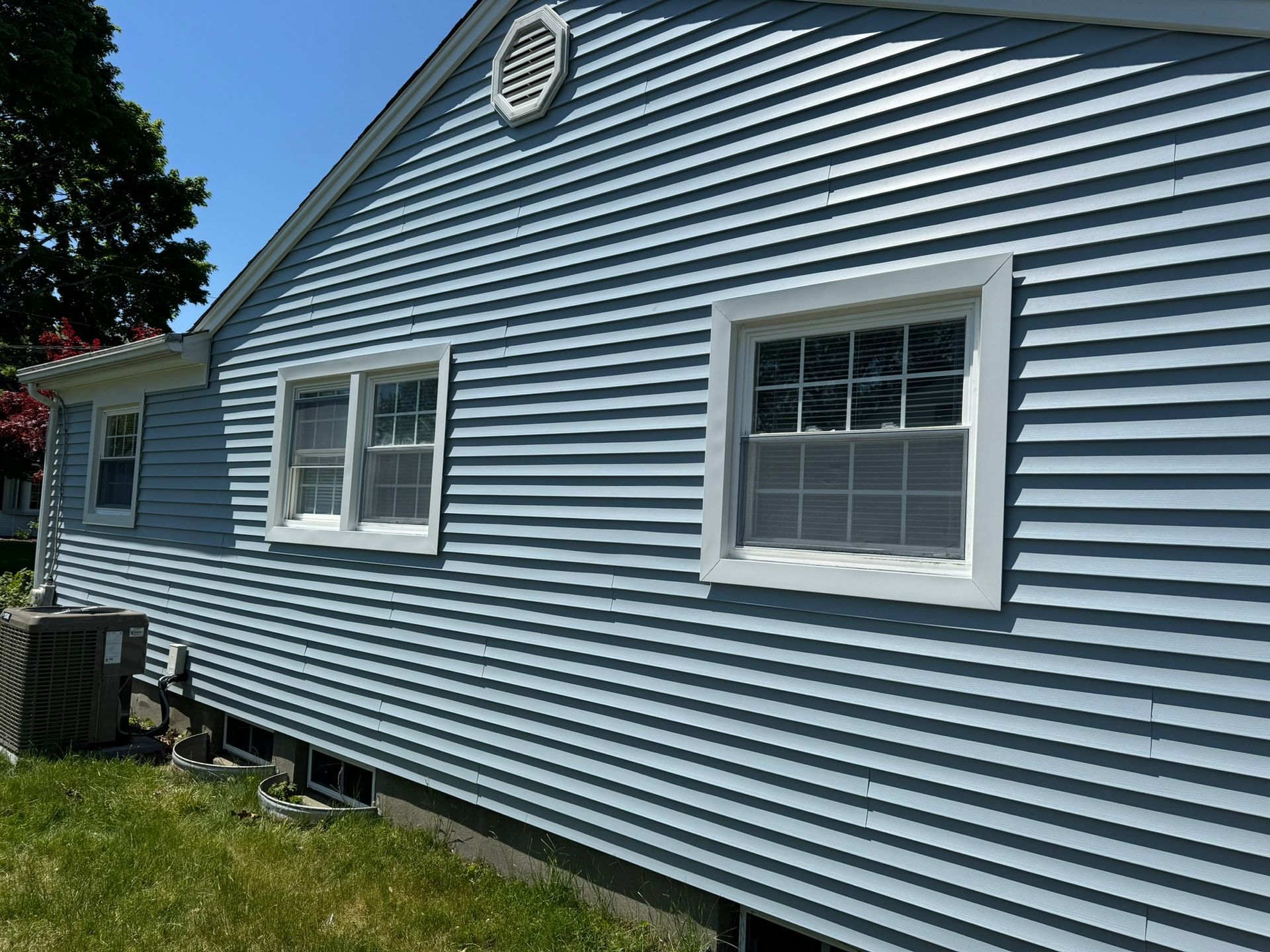 Blue-gray house siding with two windows and a round attic vent above a grassy yard.