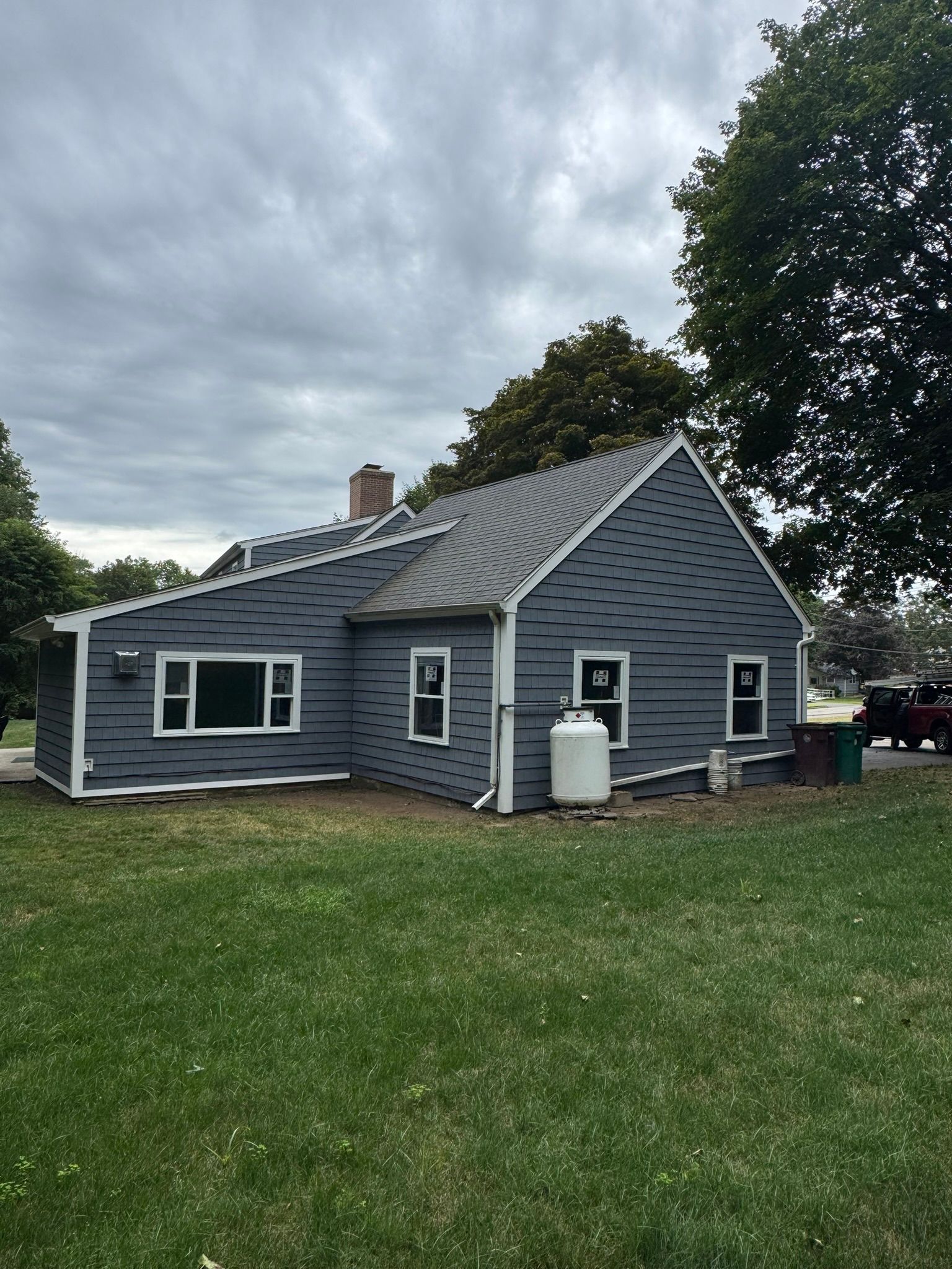 Gray house with white trim and a metal roof on a grassy lot under a cloudy sky