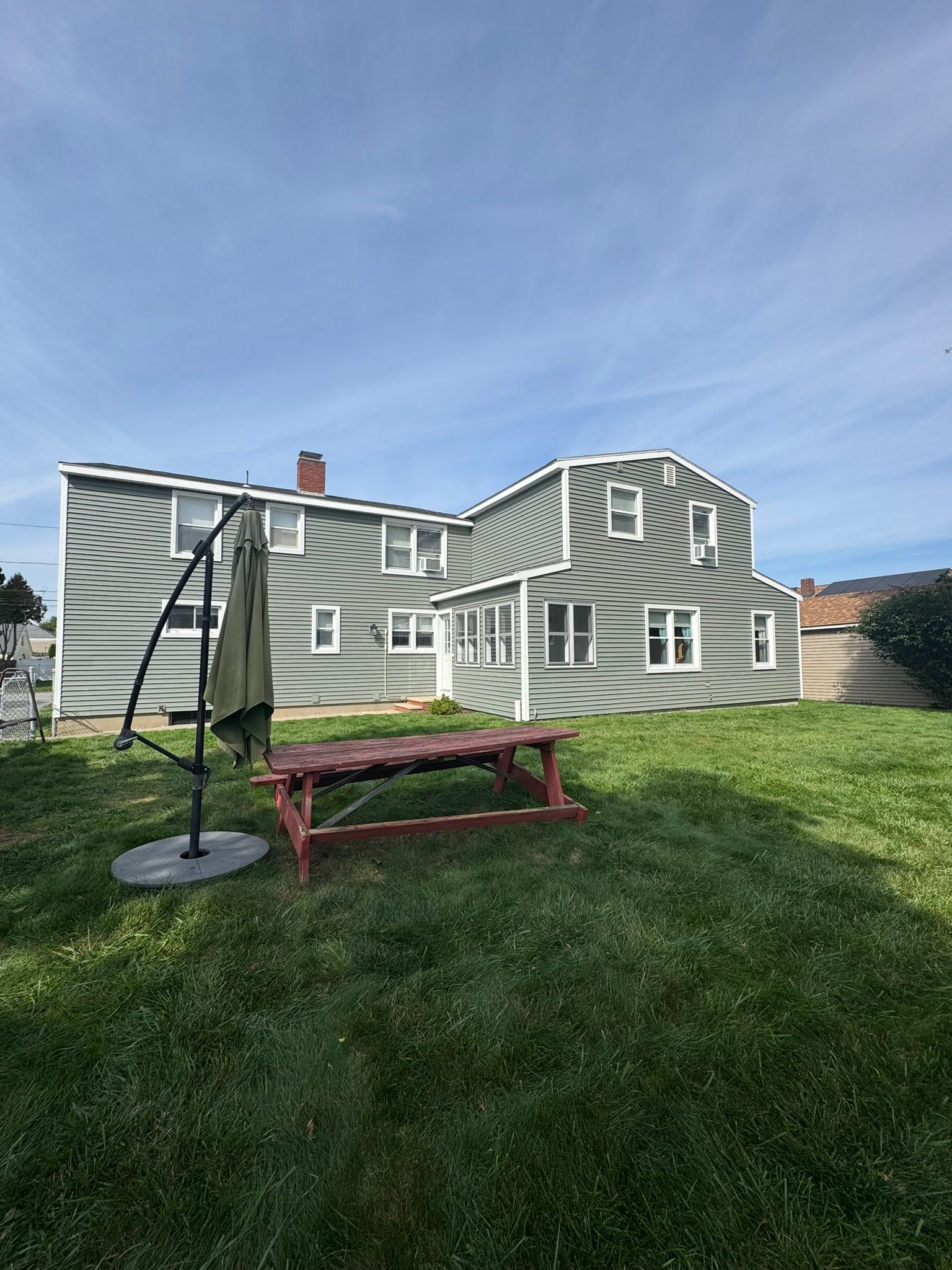 Green house with white trim and a picnic table on a grassy lawn under a blue sky.