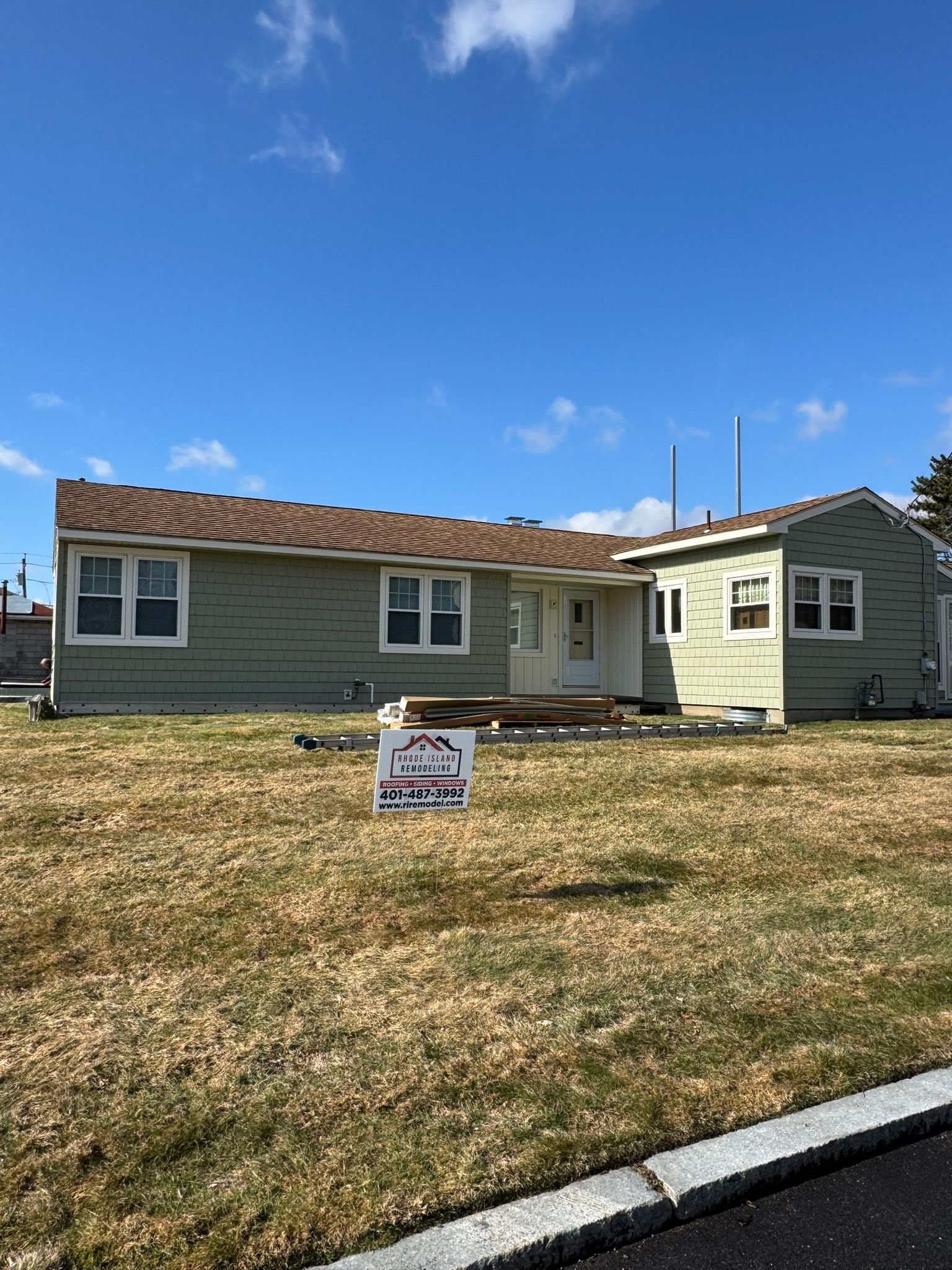 Single-story house with a for-sale sign in the front yard under a blue sky.