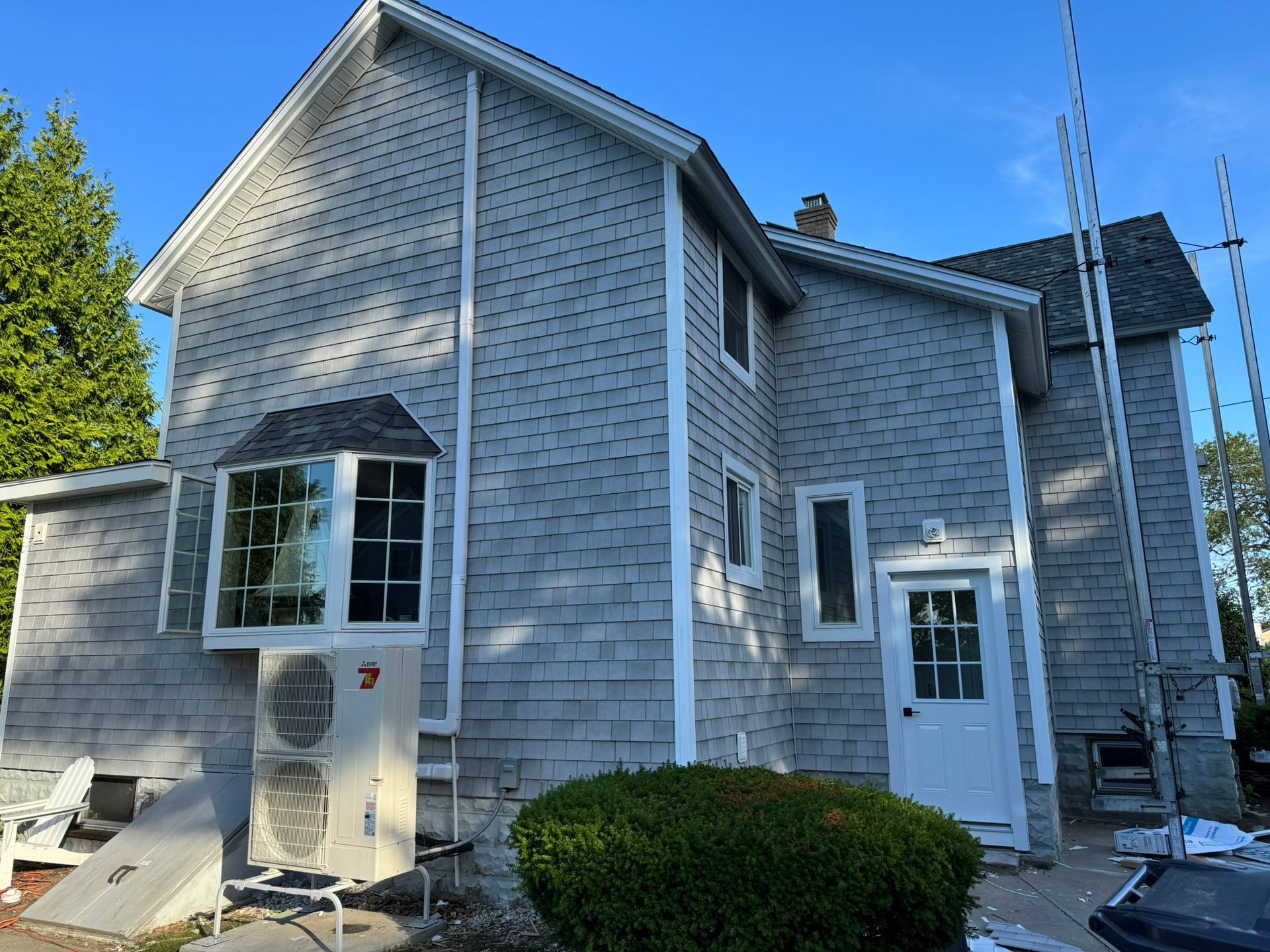 Gray two-story house with white trim, front door, and bay window under a clear blue sky