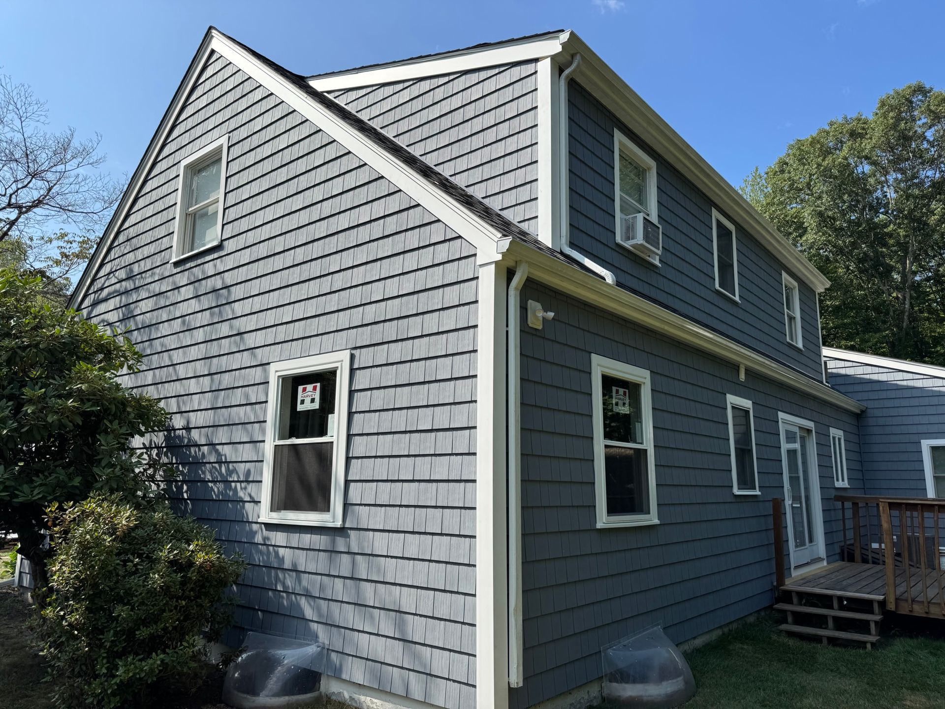 Gray house exterior with white trim and shingled siding under a blue sky, shown from the side.