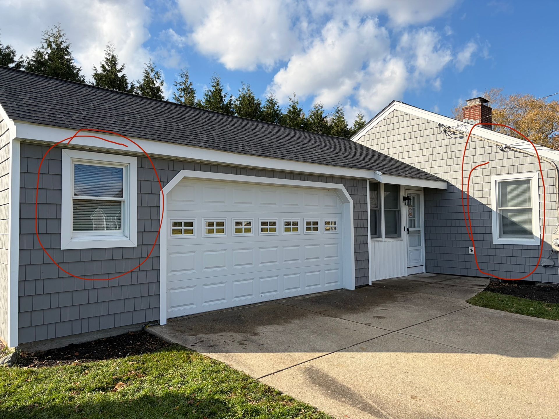 Gray house exterior with white garage door, front window, and driveway under a blue sky