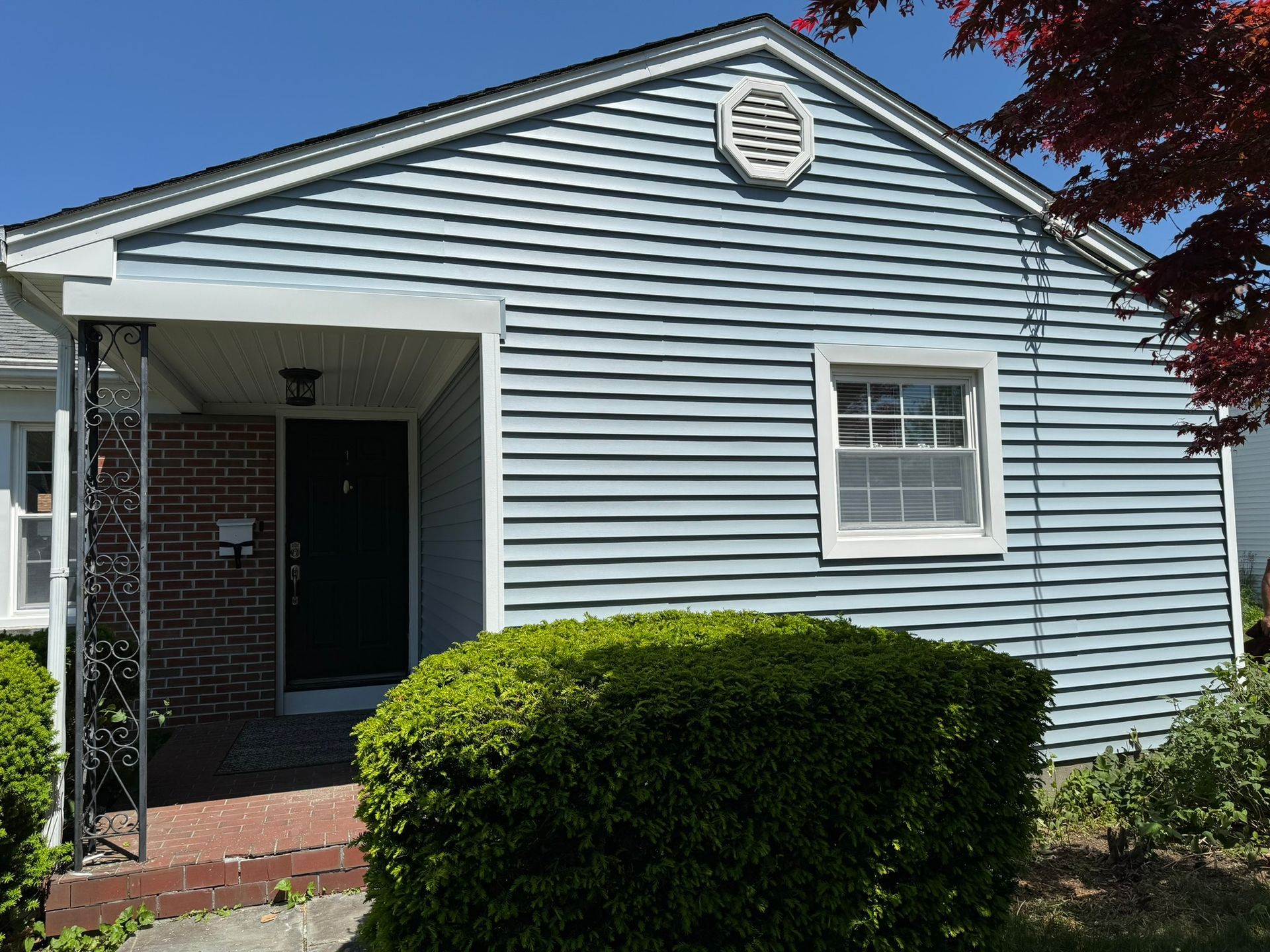 Small blue house with white trim, brick porch, and neatly trimmed hedge in front yard