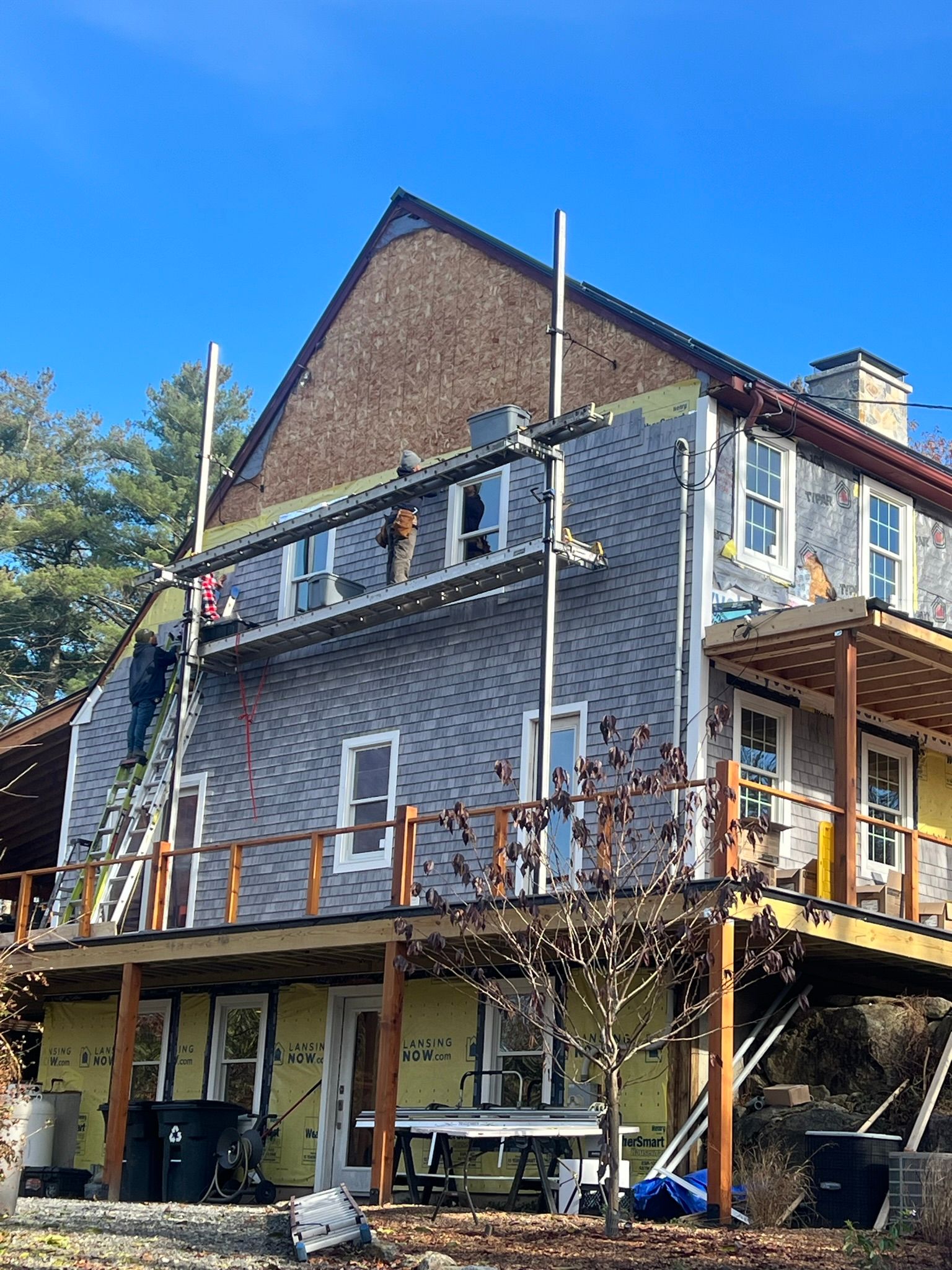 Two-story house with wood siding and a raised deck, viewed from outside on a sunny day.