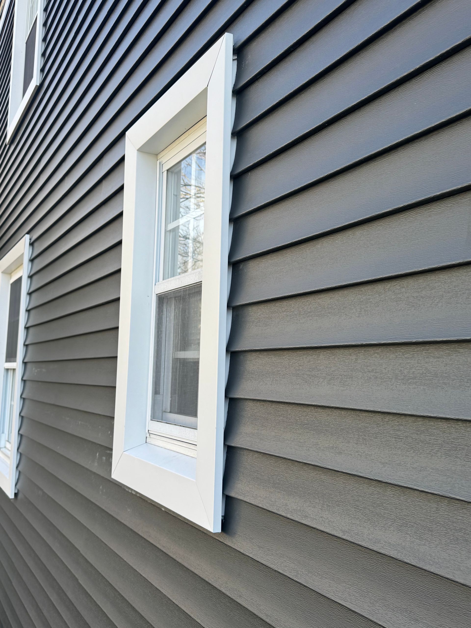 White-trimmed window on dark gray vinyl siding of a house
