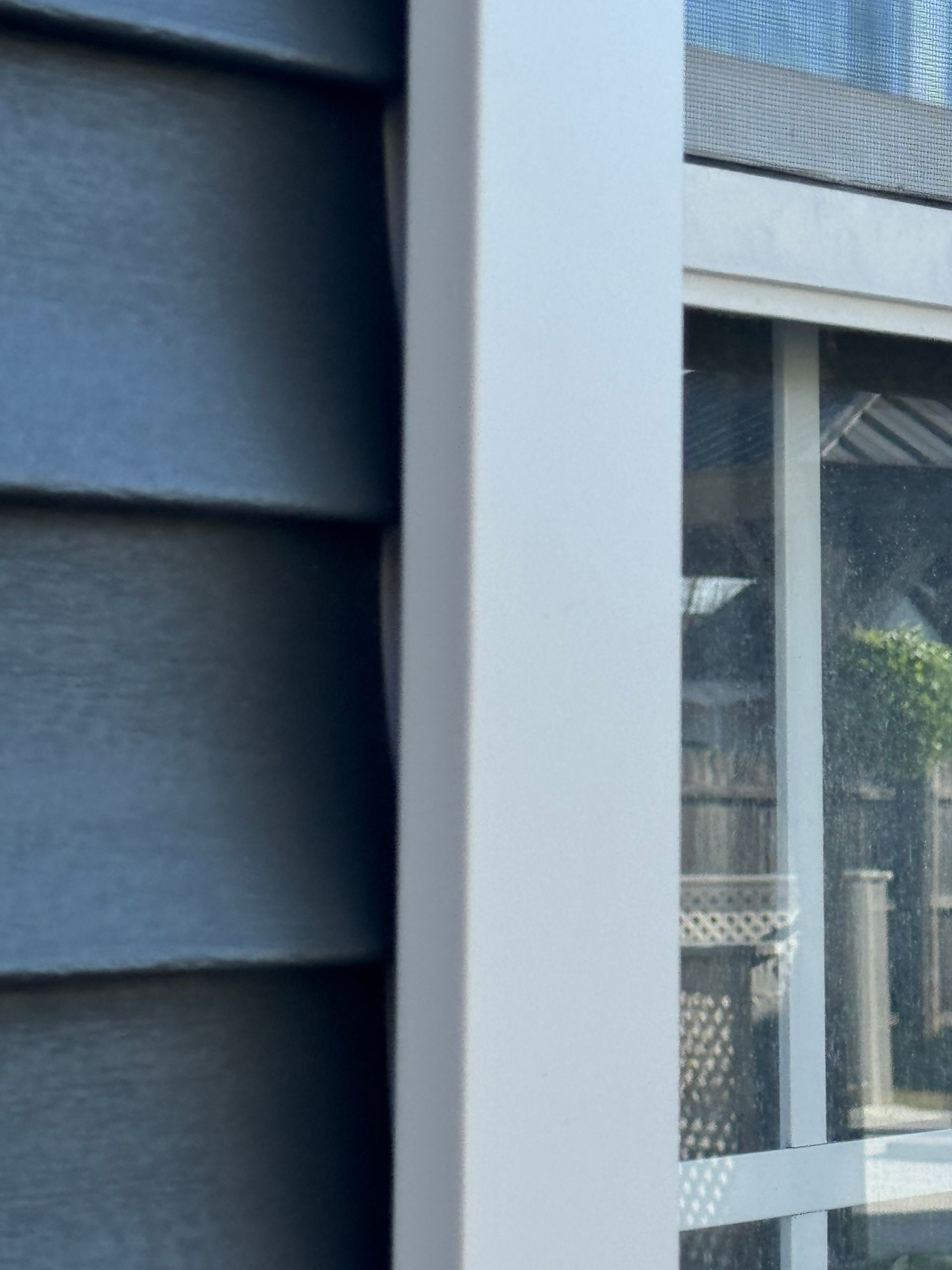 Close-up of dark blue siding beside a white-framed window with a mesh screen