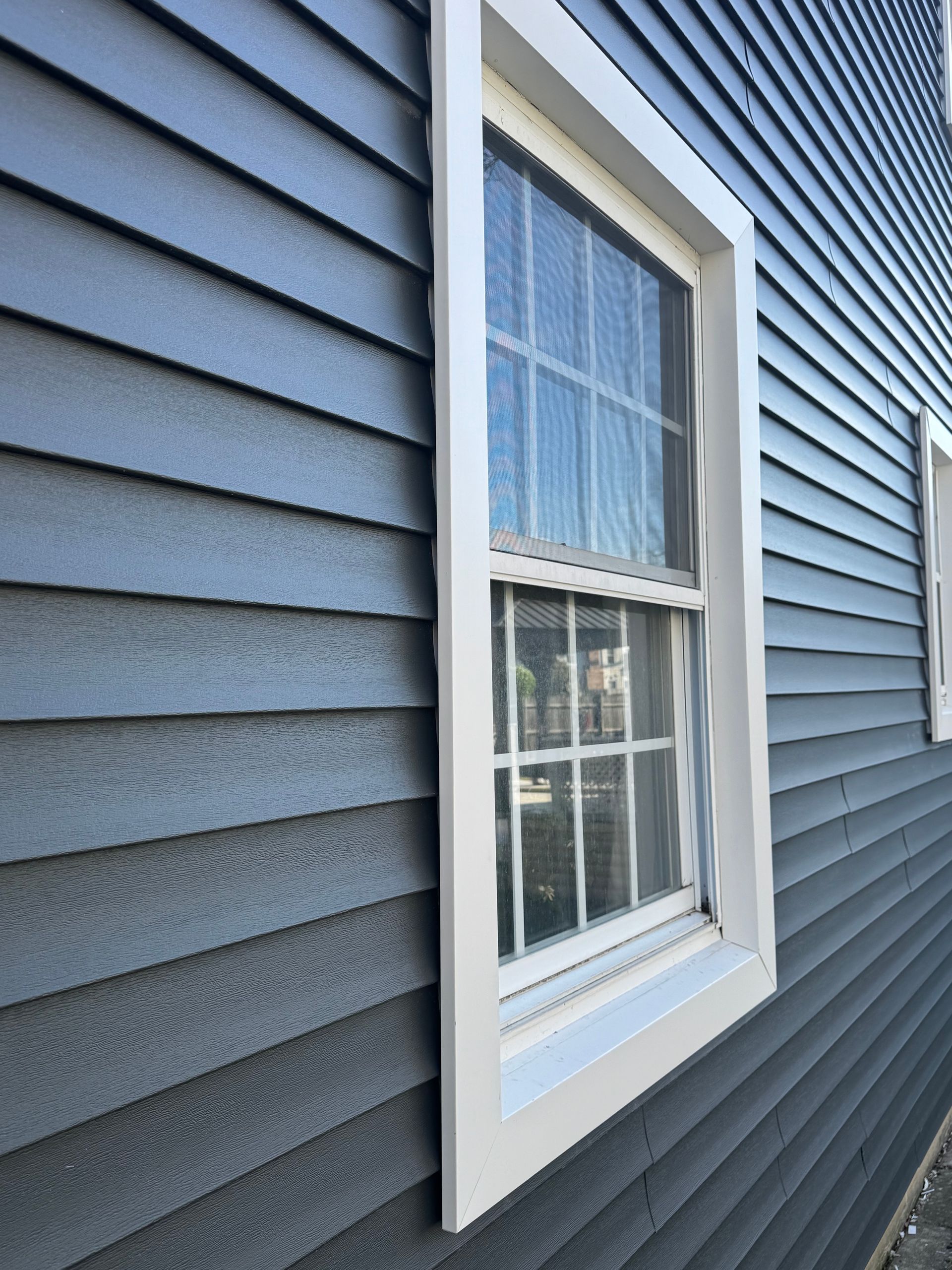 White-trimmed window on blue-gray vinyl siding with closed blinds