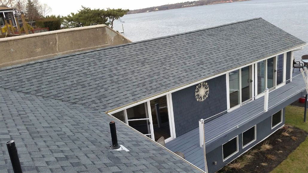 Aerial view of a gray-roofed house with a dark blue exterior and white trim near the water