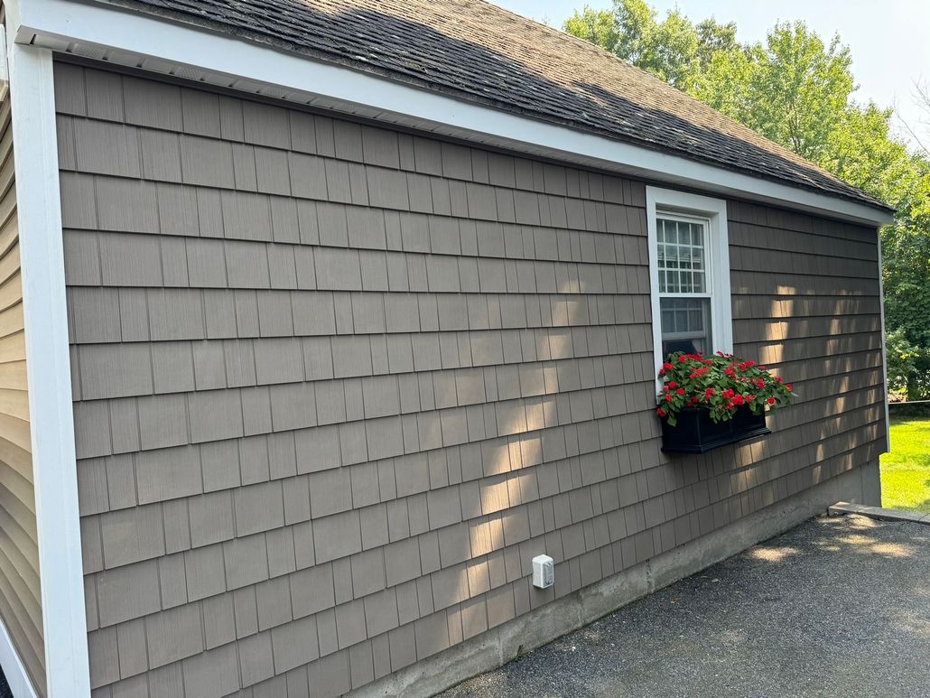 Side view of a gray house with white trim, a window box of red flowers, and a driveway beside it