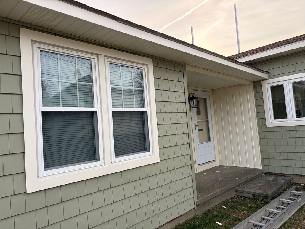 Front entrance of a small house with green siding, white trim, and a window beside the door