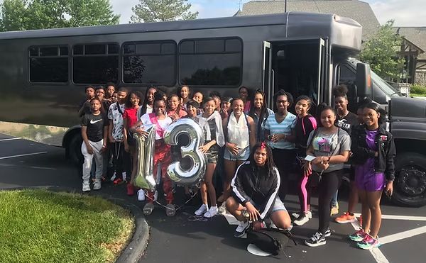 Group of young women standing in front of a dark bus holding a 