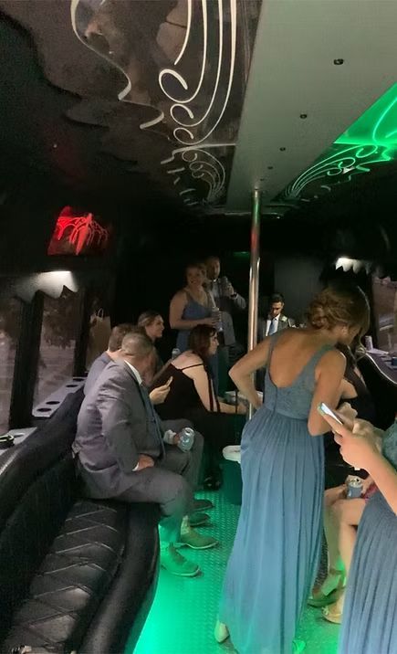 People in a limo, some in blue dresses, others in suits, celebrating. Interior lit with green and white.