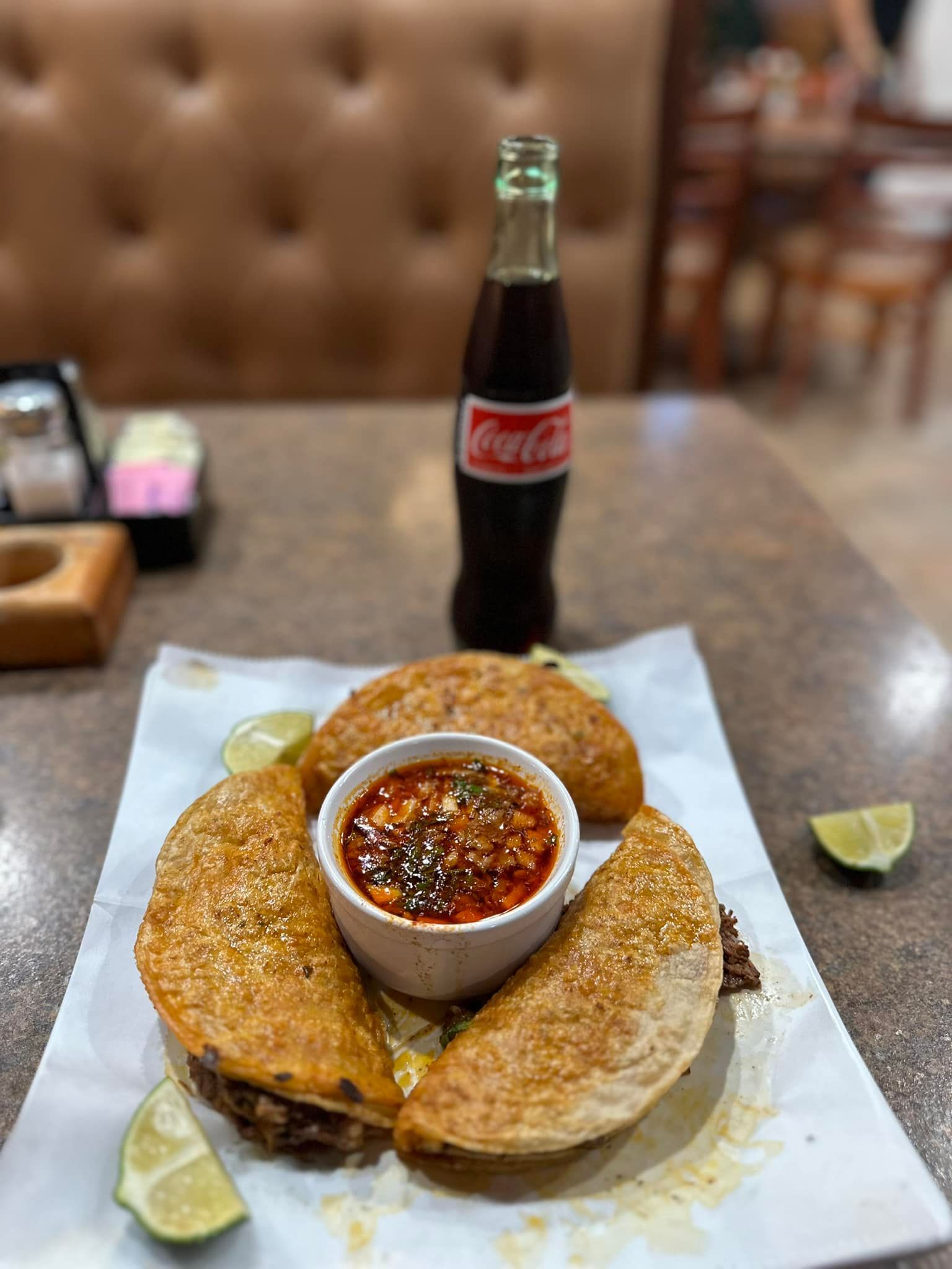 A bottle of coca cola is sitting on a table next to a plate of food.
