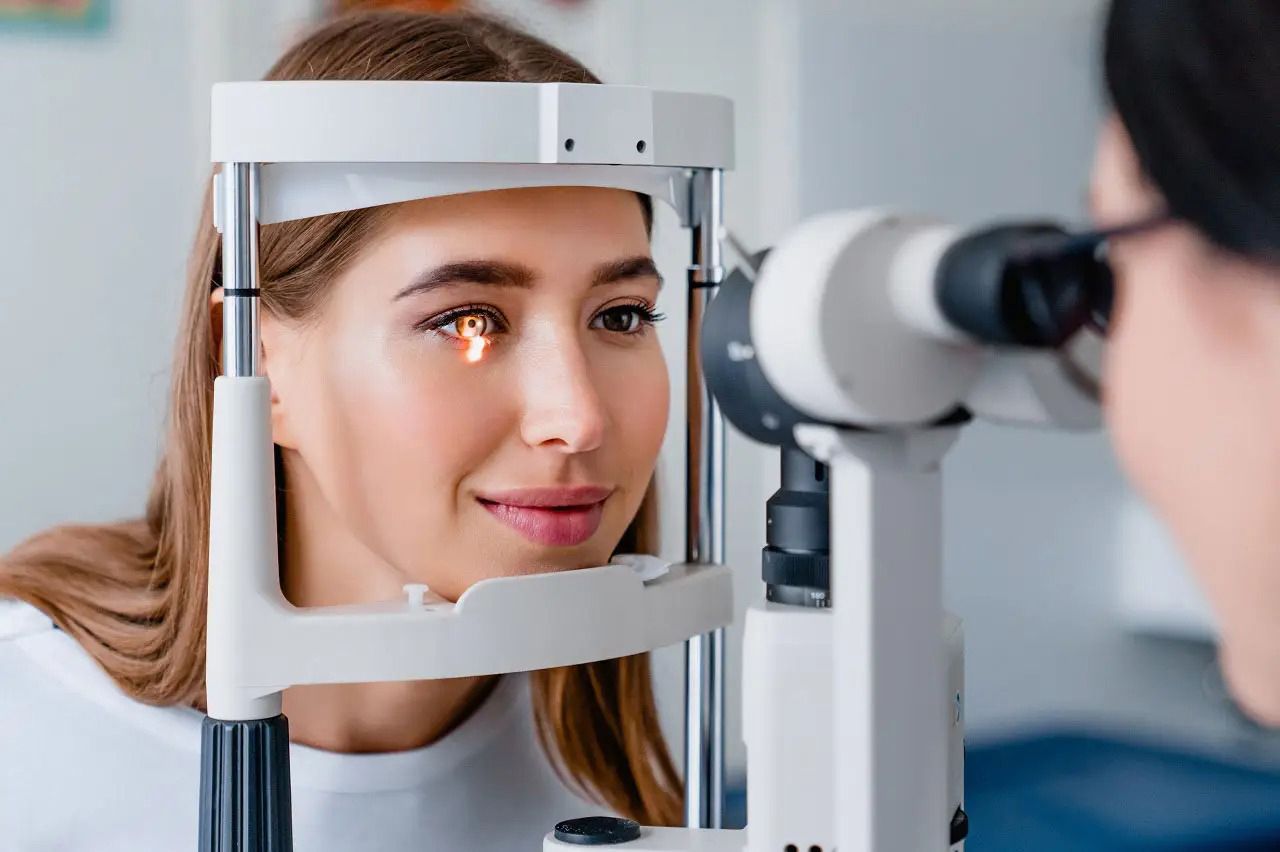 A person sitting with their chin on a rest for an eye examination using a slit lamp biomicroscope.