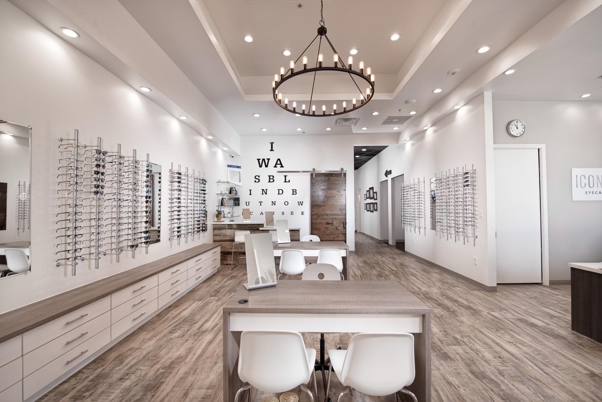 Modern optometry office featuring rows of eyeglasses on white walls, a central desk, and a large chandelier.