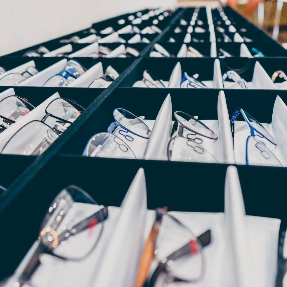 An eye-level, slightly angled view of shelves in a store containing multiple pairs of eyeglasses in individual slots.
