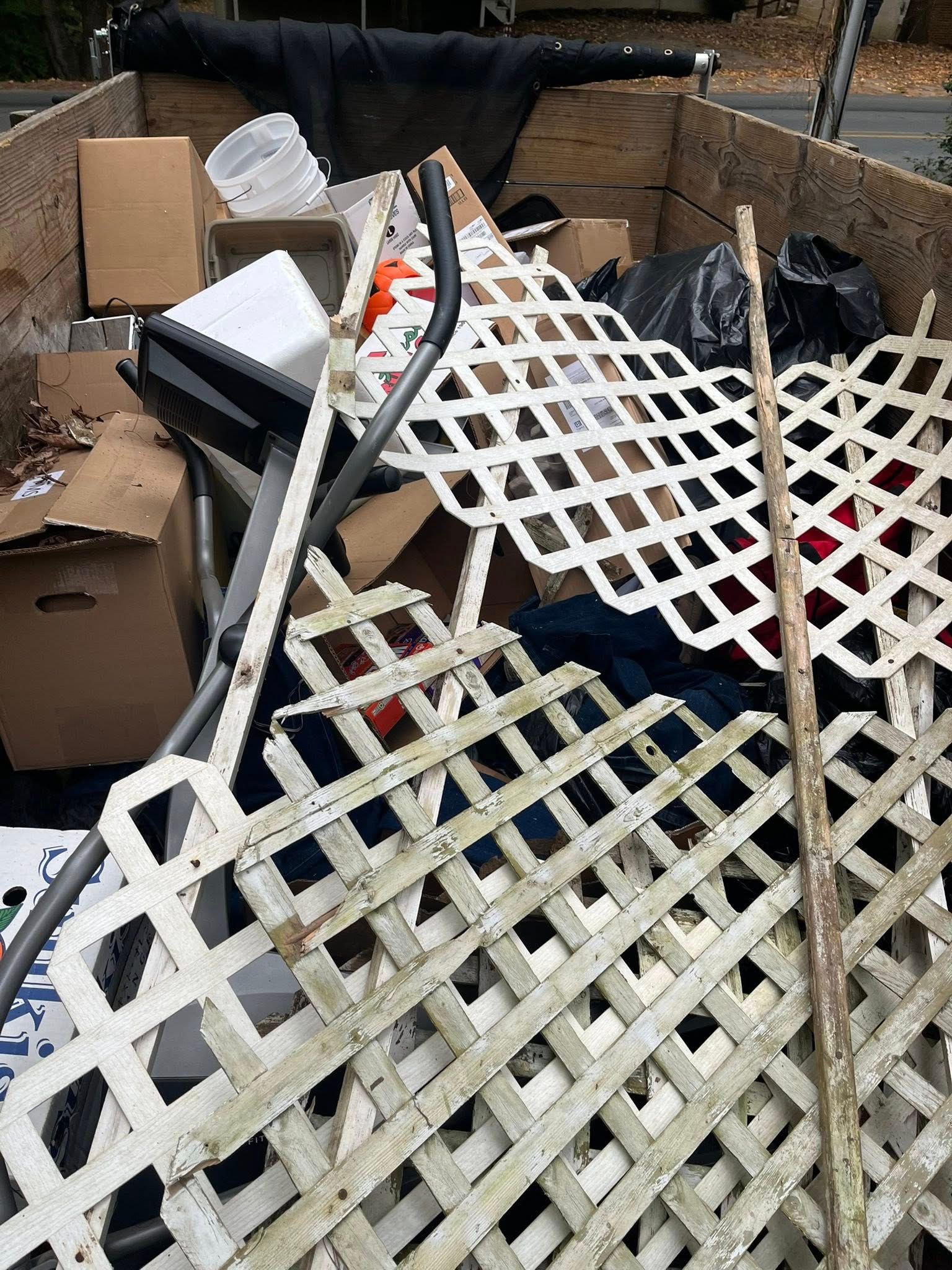 A trailer filled with junk, including white lattice panels, cardboard boxes, and a tall wooden stick.