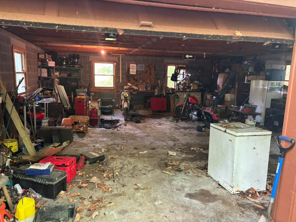 A cluttered, dimly lit garage interior with a concrete floor, tools, a motorcycle, and a chest freezer.