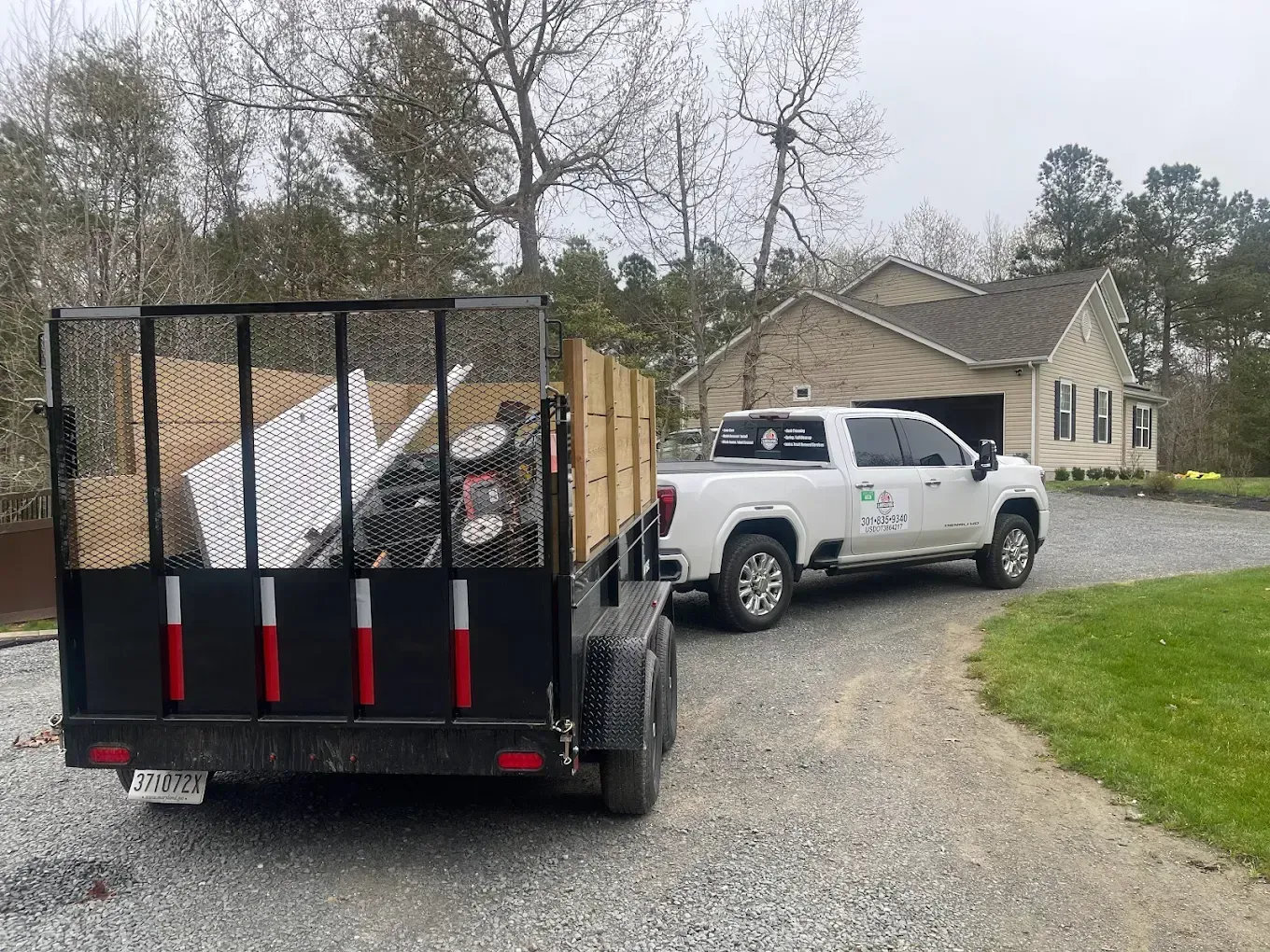 White pickup towing a debris trailer on a gravel driveway beside a house and garage