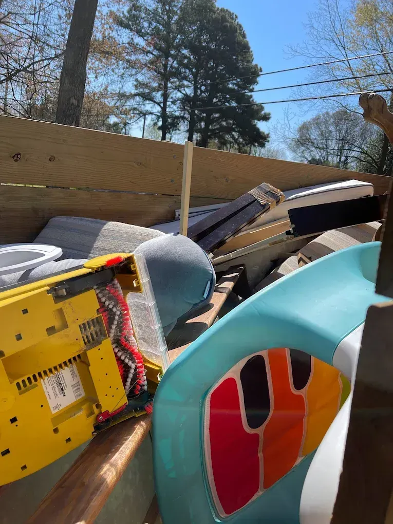 A pile of discarded household items, including a yellow vacuum base and a blue plastic chair, sitting in a truck bed.