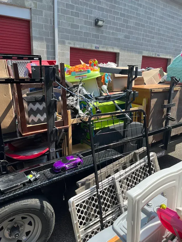 A flatbed trailer loaded with assorted household items, including a green baby walker, plastic bins, and a toy car.