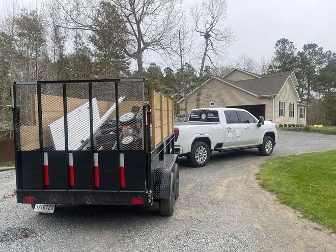 A white pickup truck with a large, loaded black utility trailer parked on a gravel driveway in front of a house.